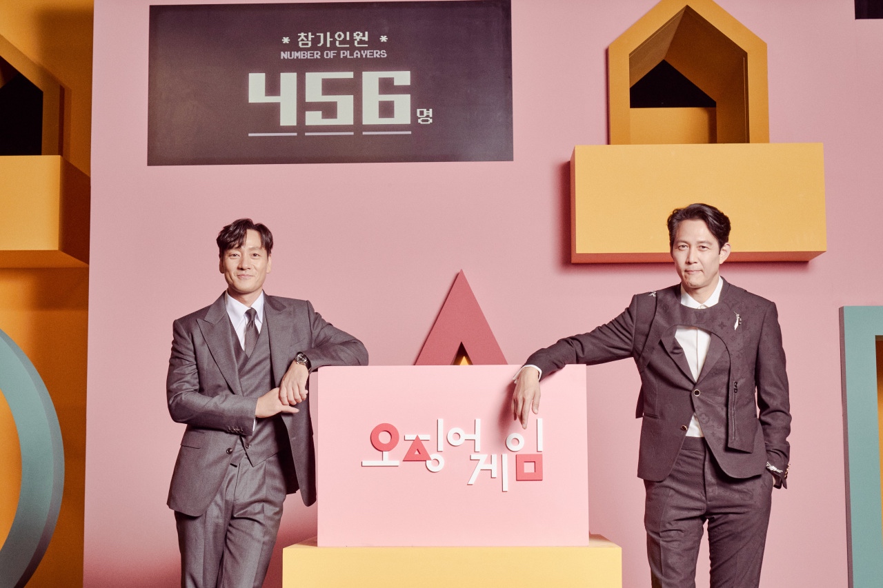 Park Hae-Soo and Lee Jung-Jae for Netflix's 'Squid Game' wearing black suits standing in pink furnished room