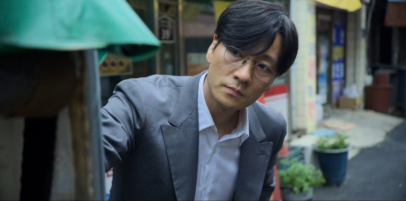 Park Hae-soo as Cho Sang-woo in 'Squid Game' episode 2 wearing grey suit and glasses