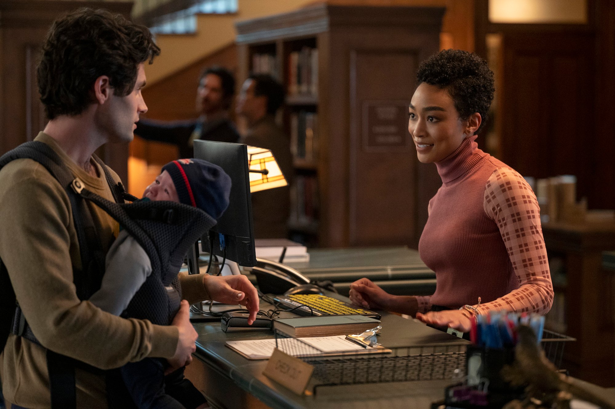 Penn Badgley, and Tati Gabrielle talking in a library in 'You' Season 3.