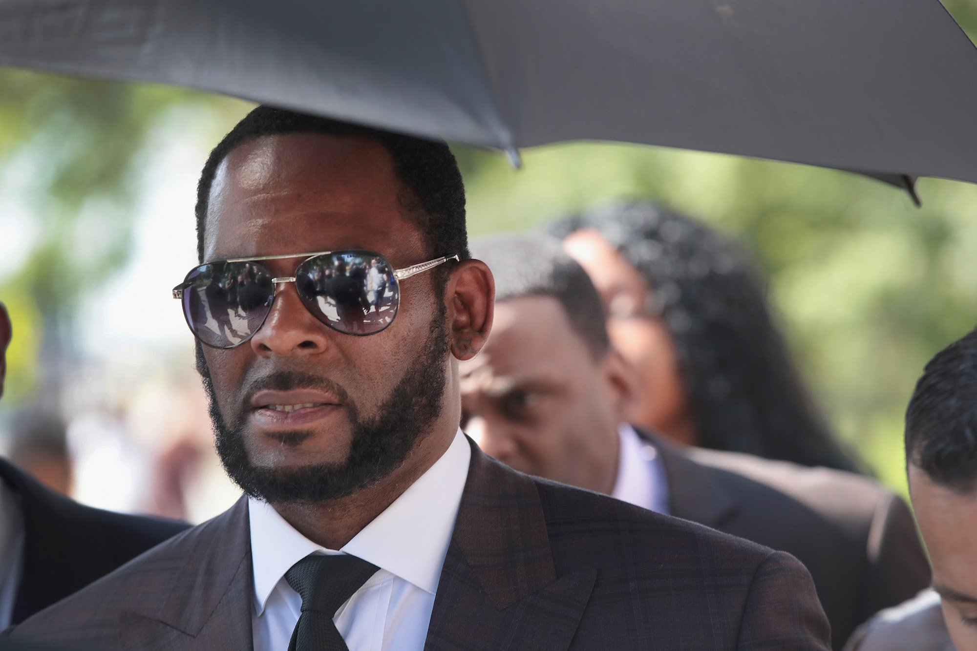 R. Kelly stands under an umbrella on his way to court