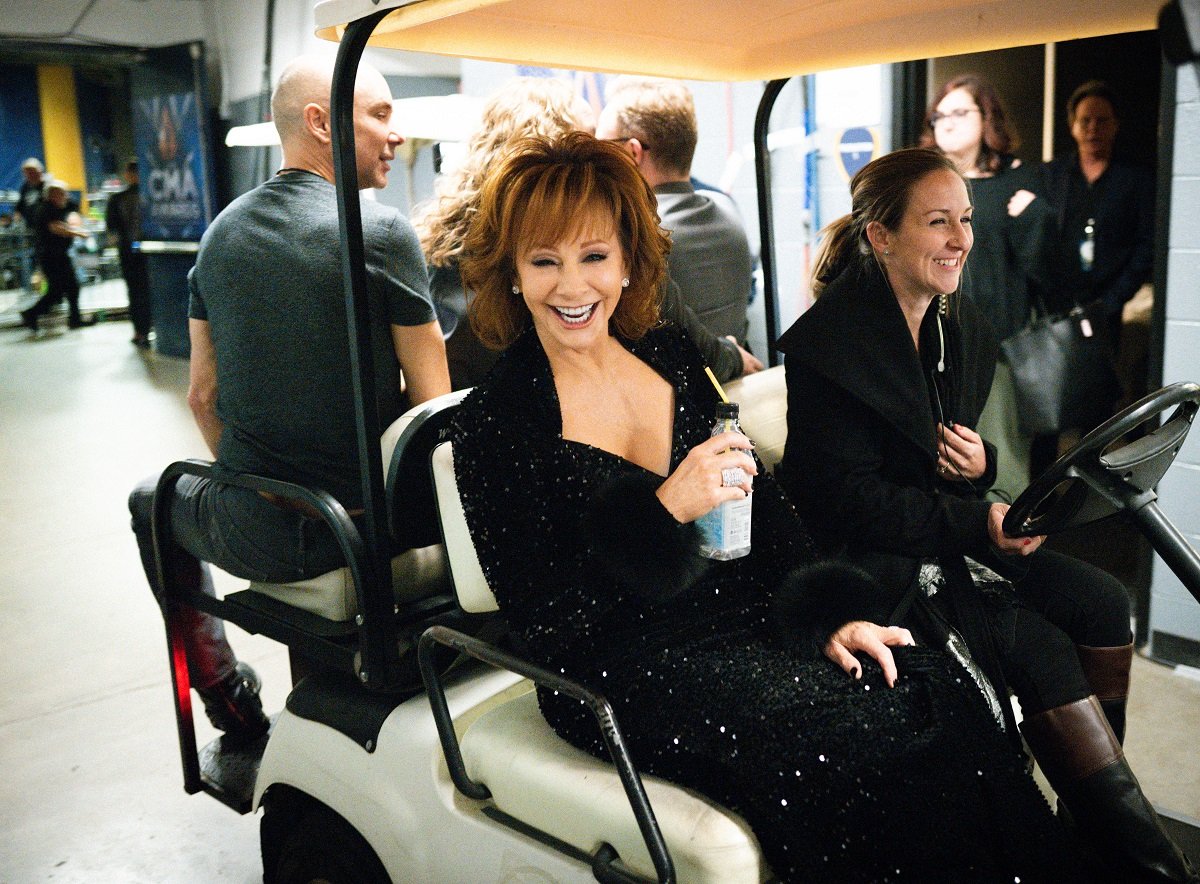 Reba McEntire laughing while riding in a golf cart backstage at an award show