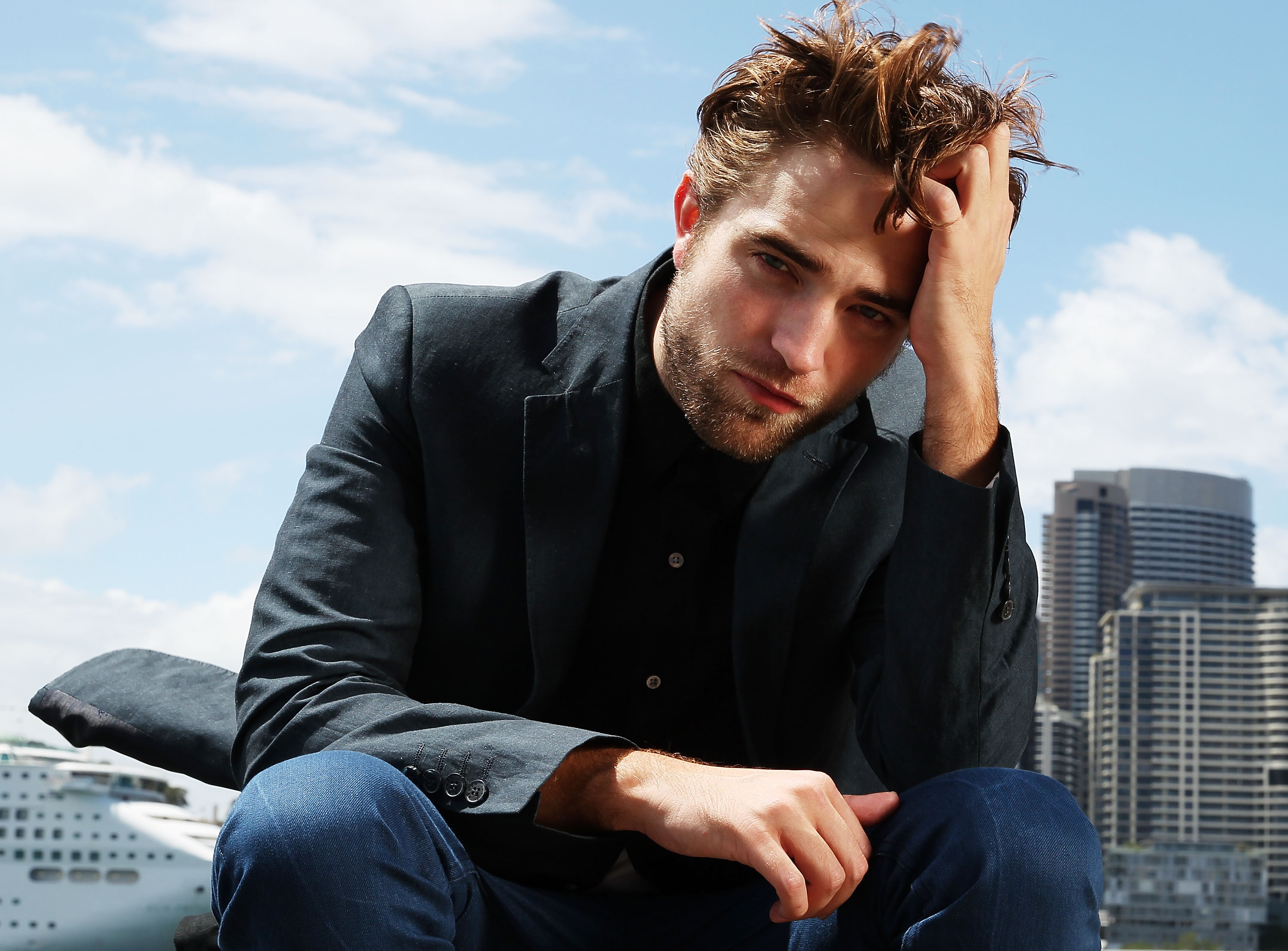 'The Batman' star Robert Pattinson wears a black suit over a black button up shirt and jeans.