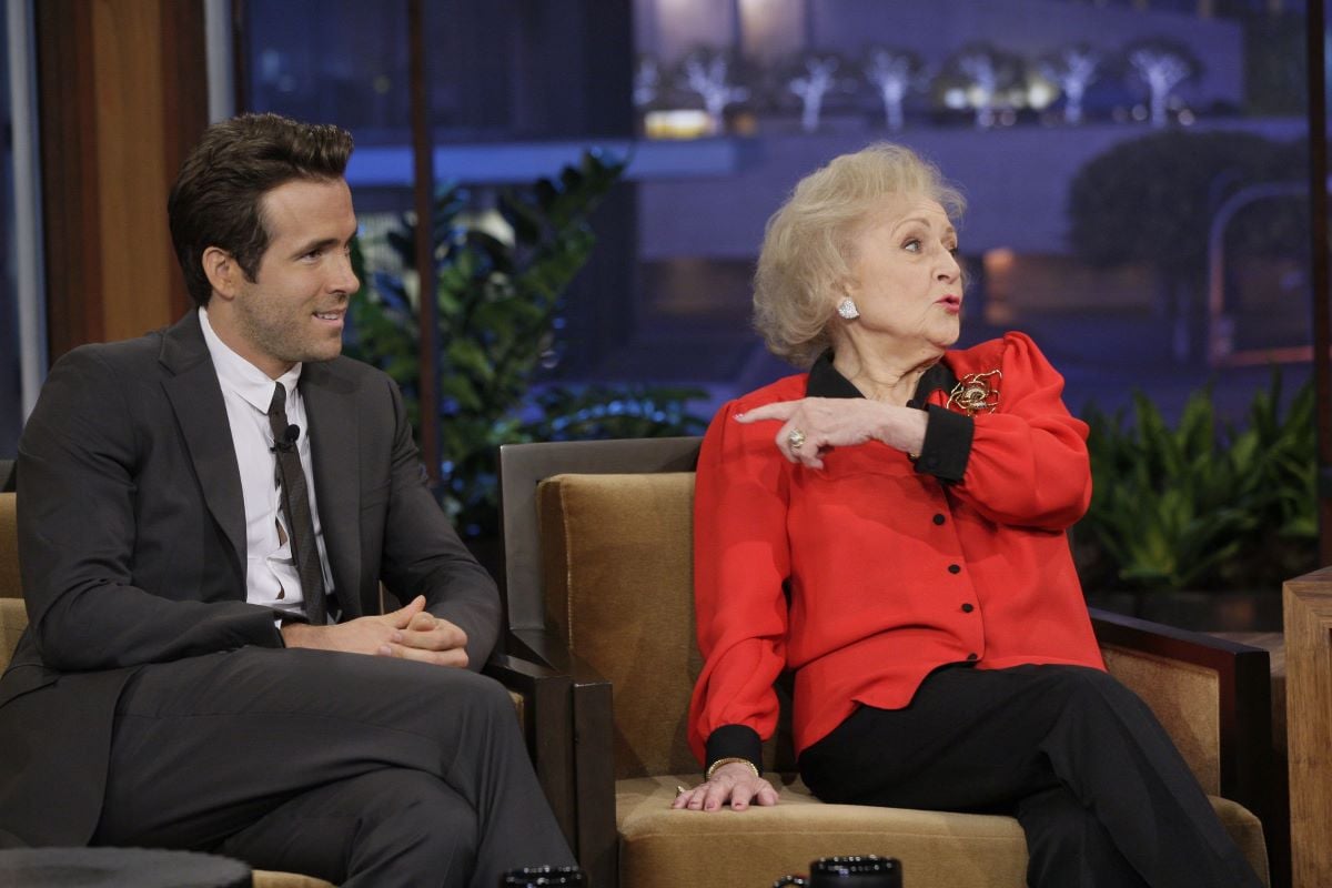 Ryan Reynolds in a suit, Betty White sitting next to him in red, pointing at him