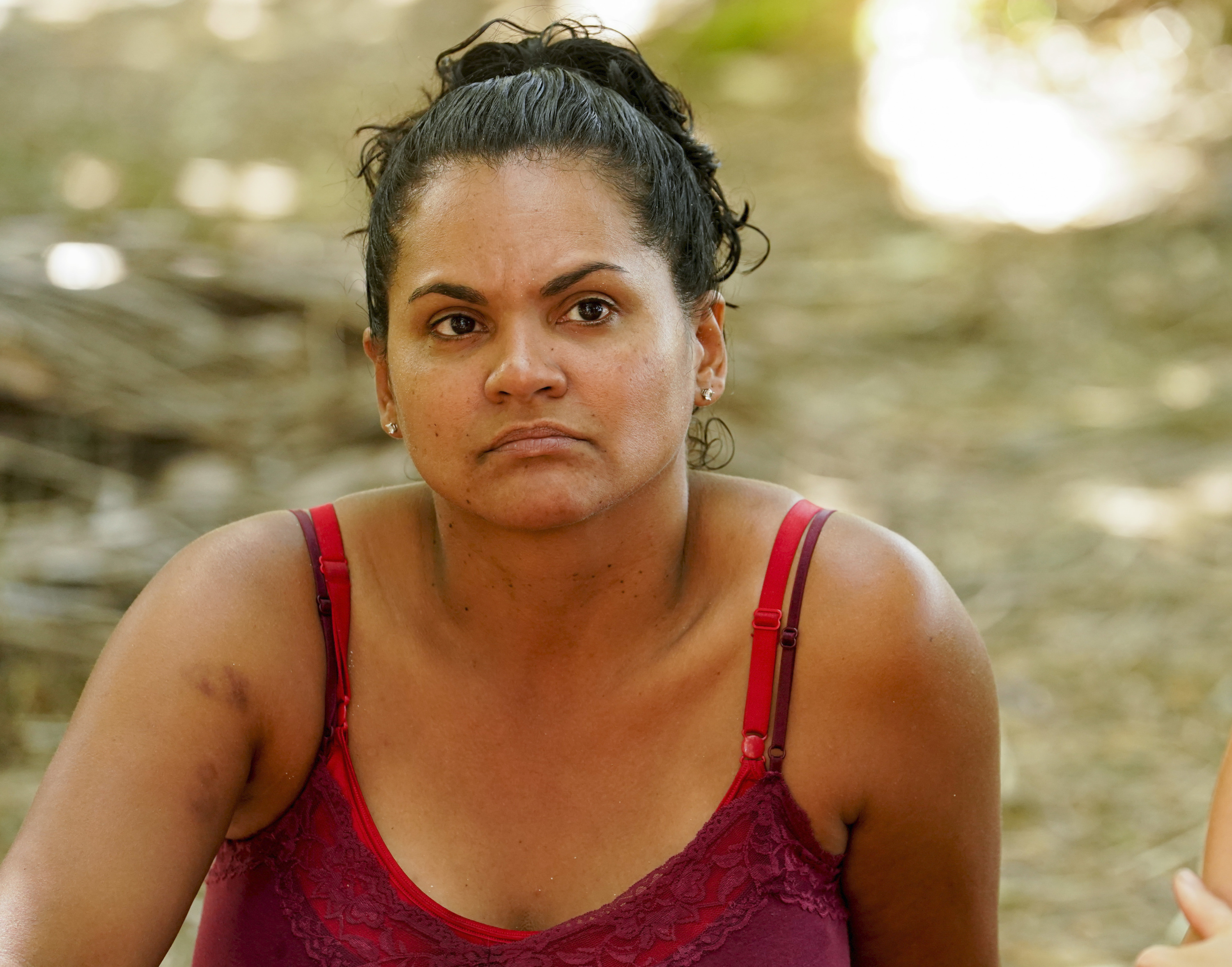 Sandra Diaz-Twine on 'SURVIVOR: WINNERS AT WAR' wears a red top and sits on the ground.