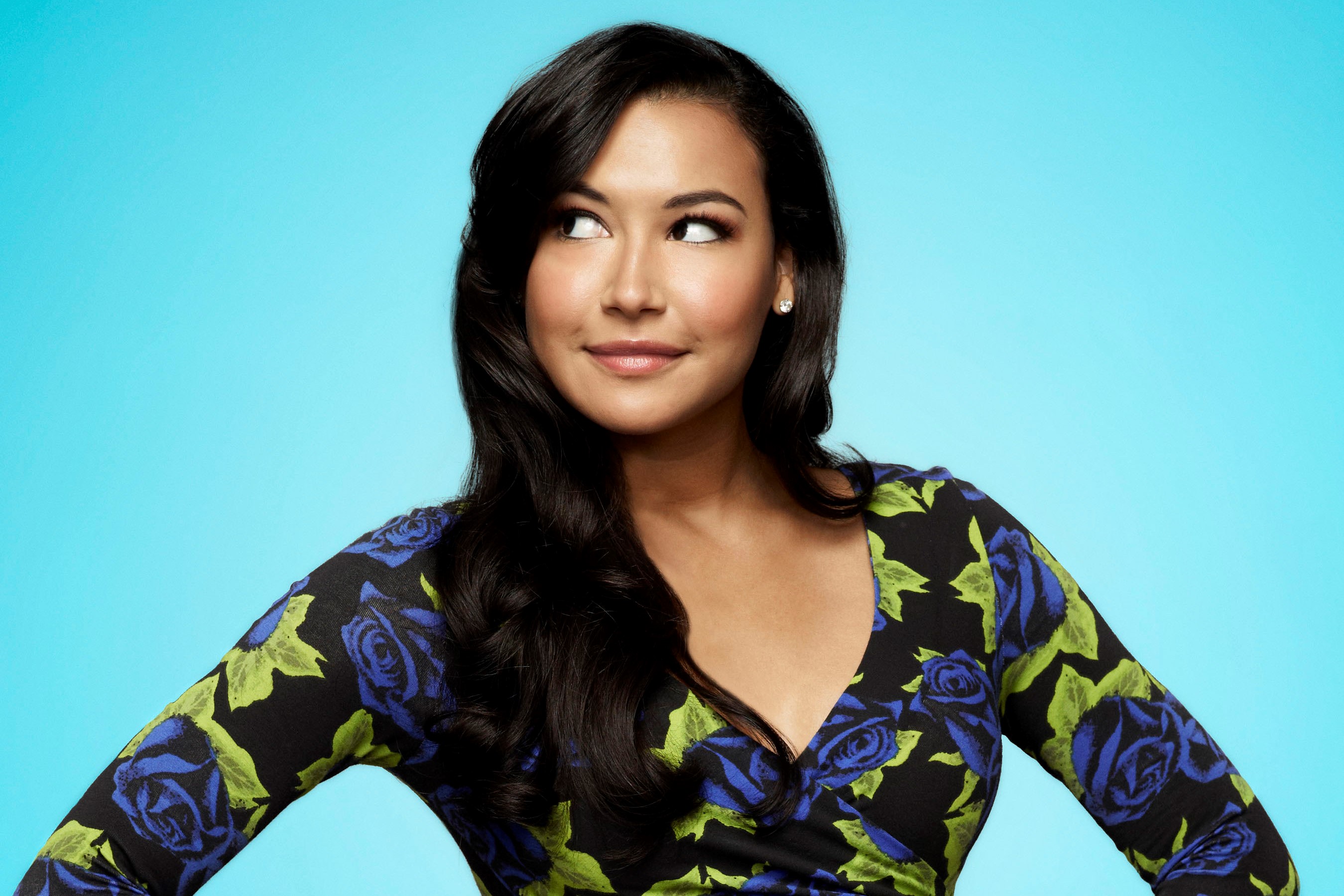 'Glee' star Naya Rivera wears a black long-sleeved shirt with blue roses and green leaves on it. 'Glee' is leaving Netflix in Nov. 2021, so fans will have to look elsewhere to watch Rivera play Santana Lopez.