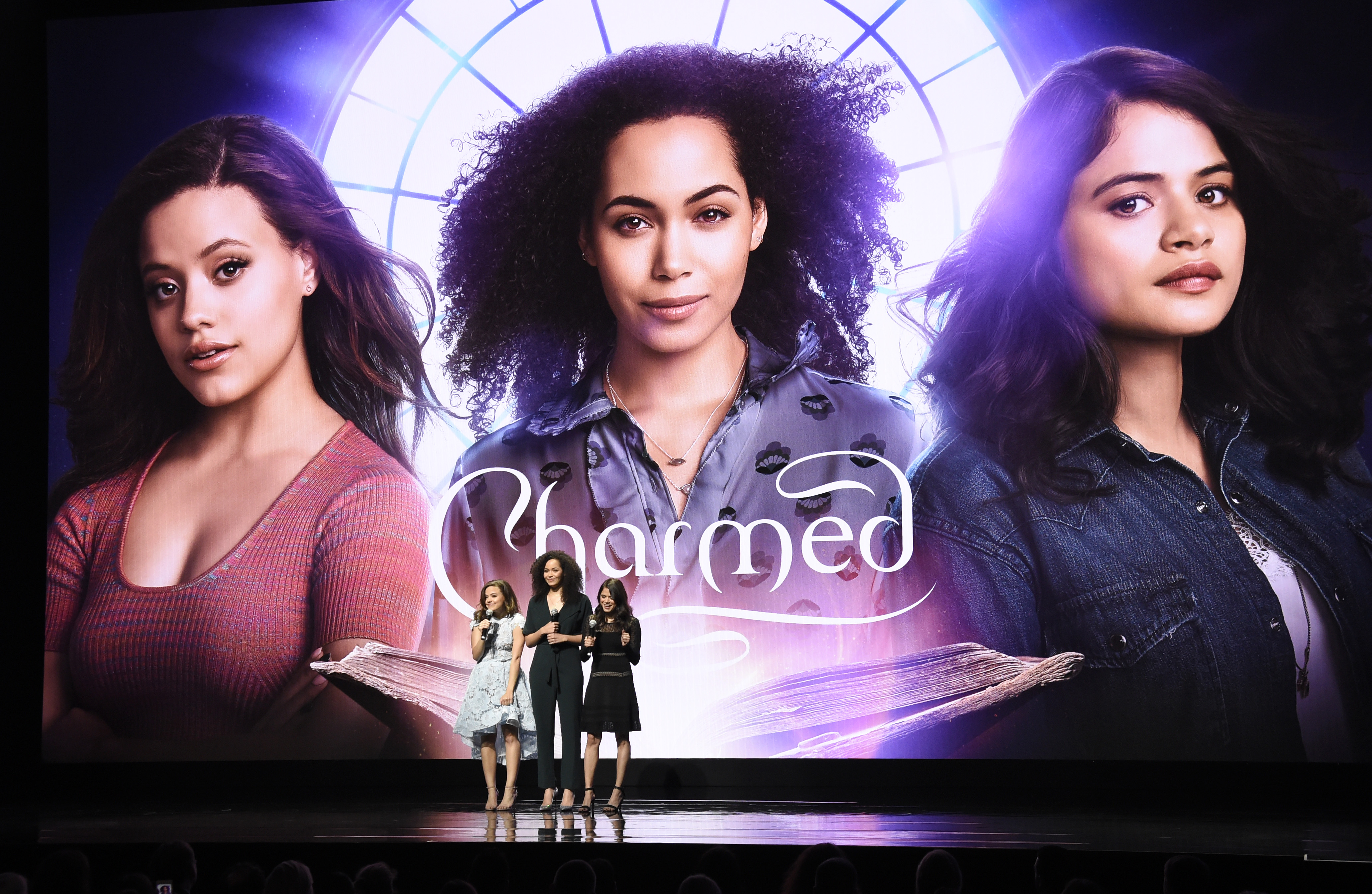 Sarah Jeffrey, Melonie Diaz, and Madeline Mantock stand on stage in front of a poster for 'Charmed.'