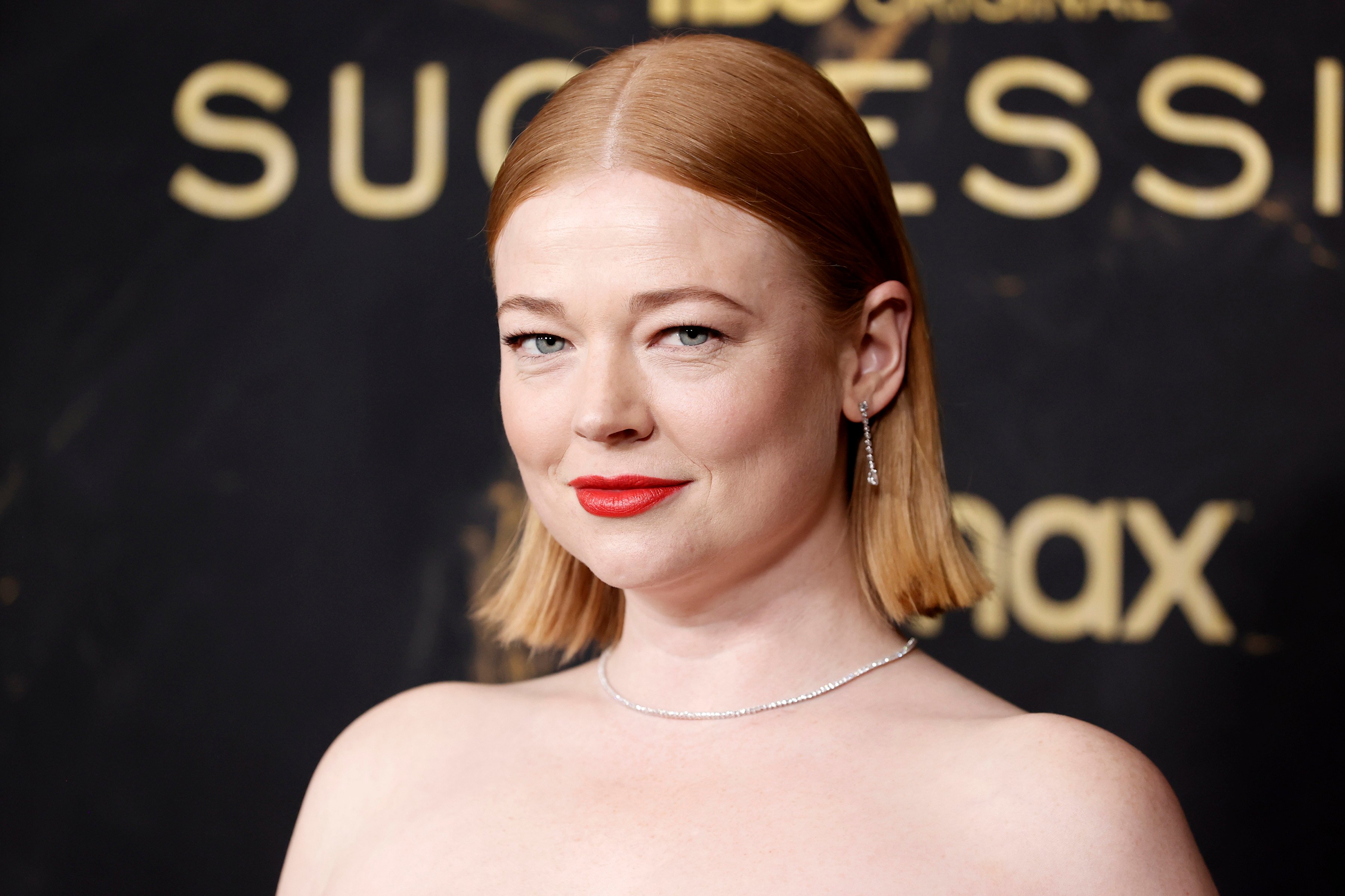 Succession cast member Sarah Snook wears a strapless dress and red lipstick.