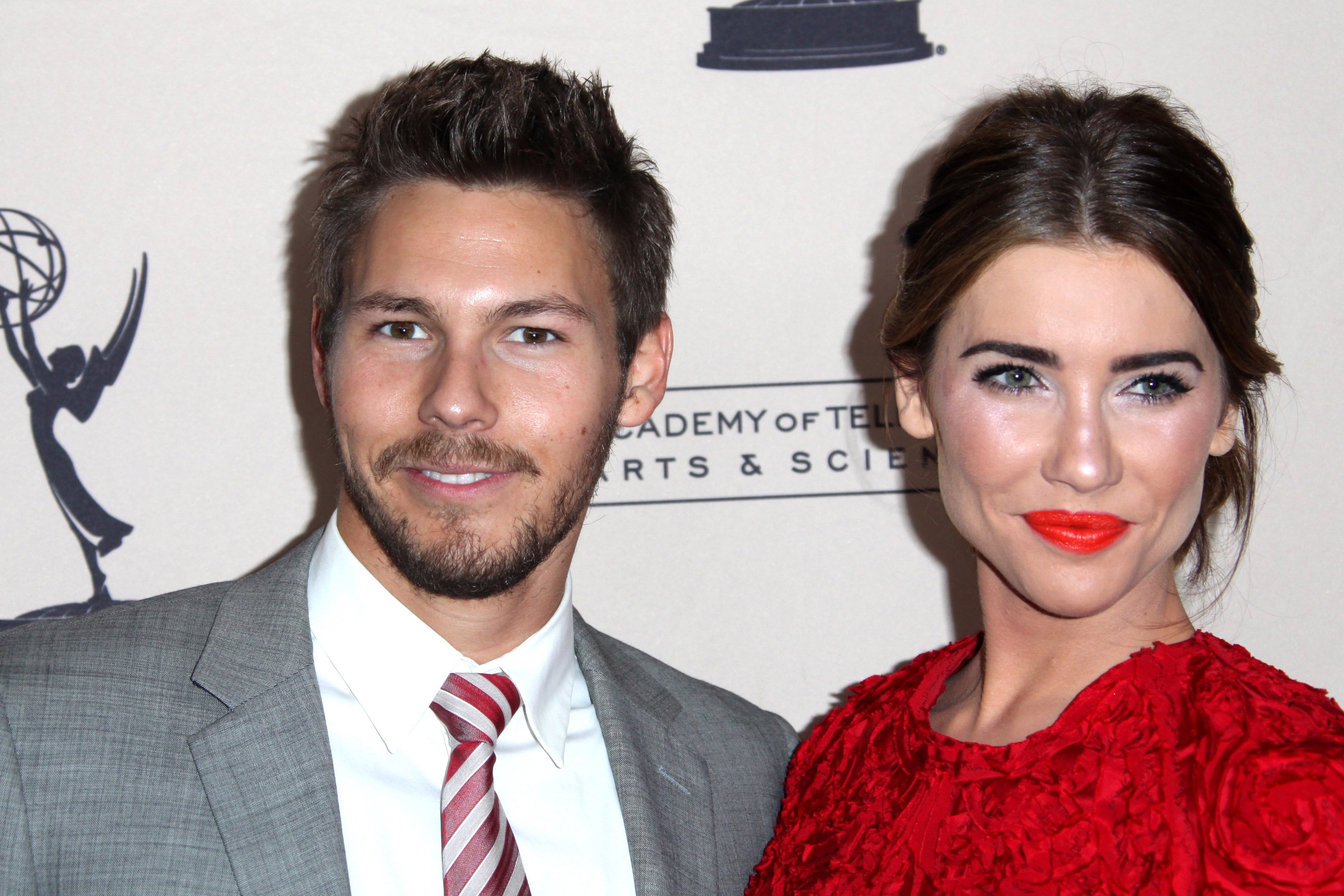 'The Bold and the Beautiful' actor Scott Clifton in a grey suit and Jacqueline MacInnes Wood in a red dress pose for a photo together.