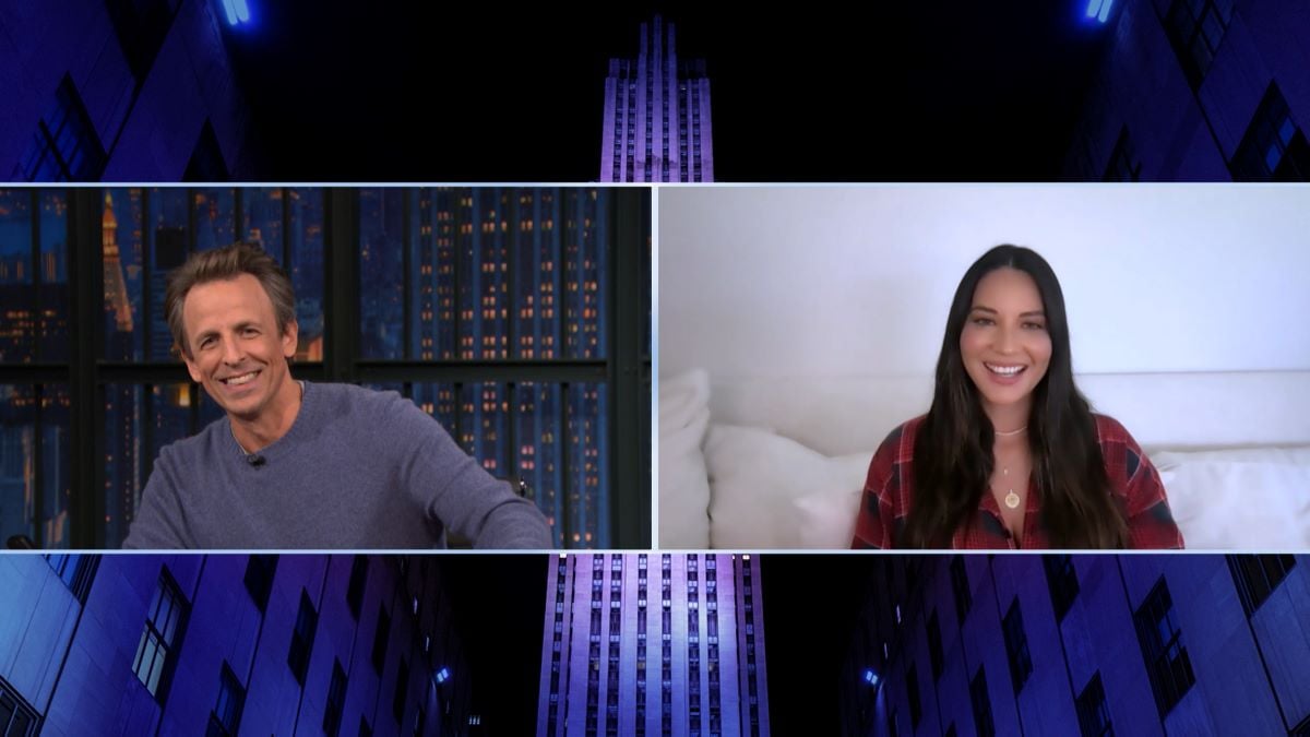 (L) Seth Meyers in a blue sweater (R) Olivia Munn in a plaid shirt -- both smiling on video screens