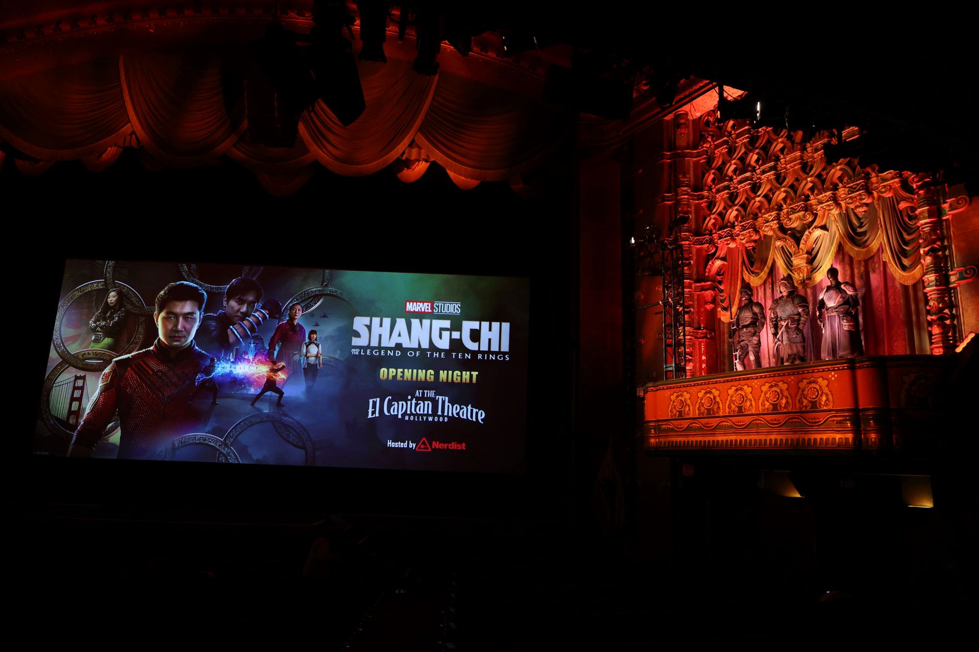 'Shang-Chi and The Legend Of The Ten Ring' projected on the screen in a theater with costumes displayed on the right.