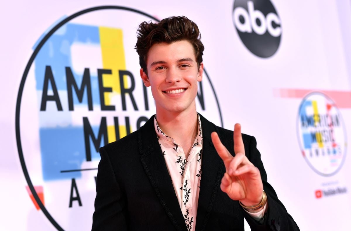 Shawn Mendes smiling in a suit and giving a peace sign