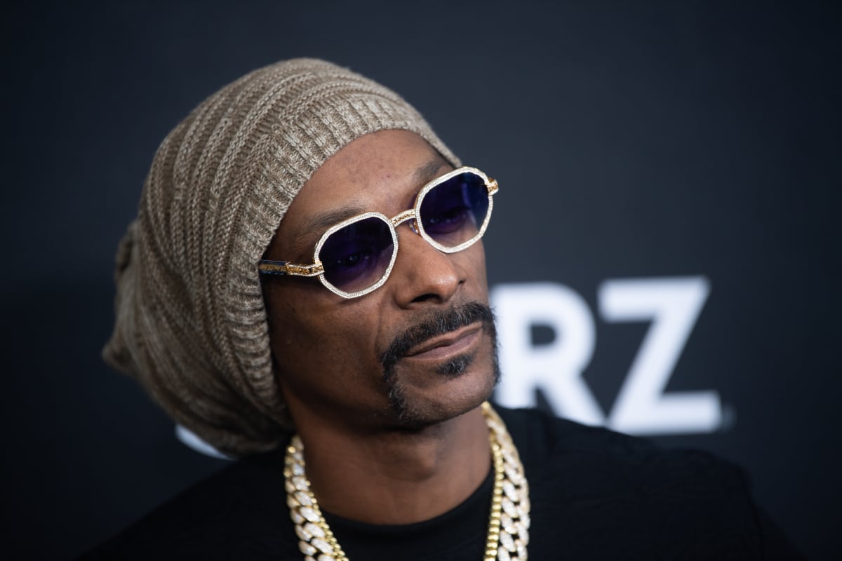 Snoop Dogg wears sunglasses, a chain, a black shirt and a knit hat.