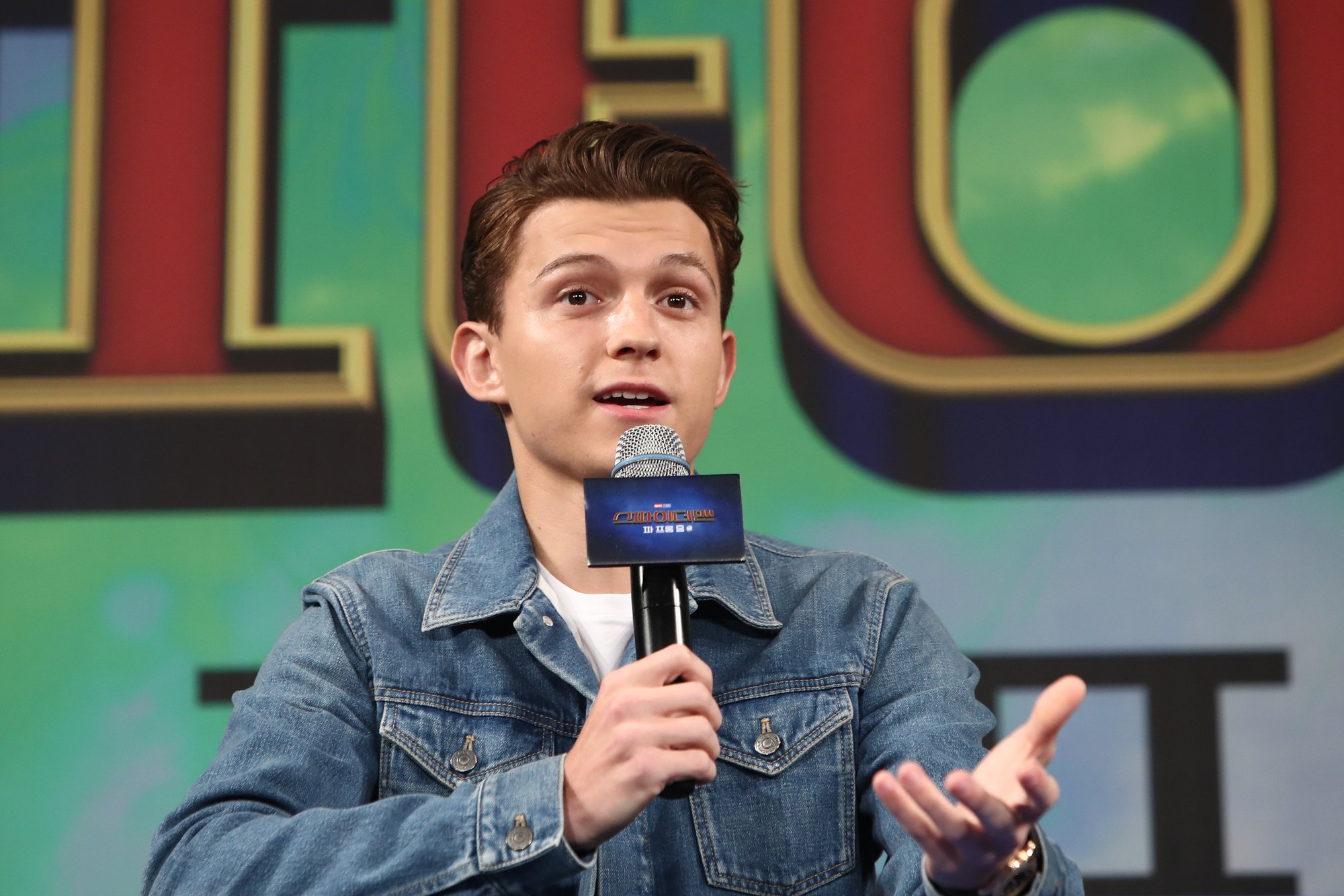 'Spider-Man: No Way Home' star Tom Holland, who will take on multiple villains in the upcoming film. He's sitting on a panel and speaking into a microphone.