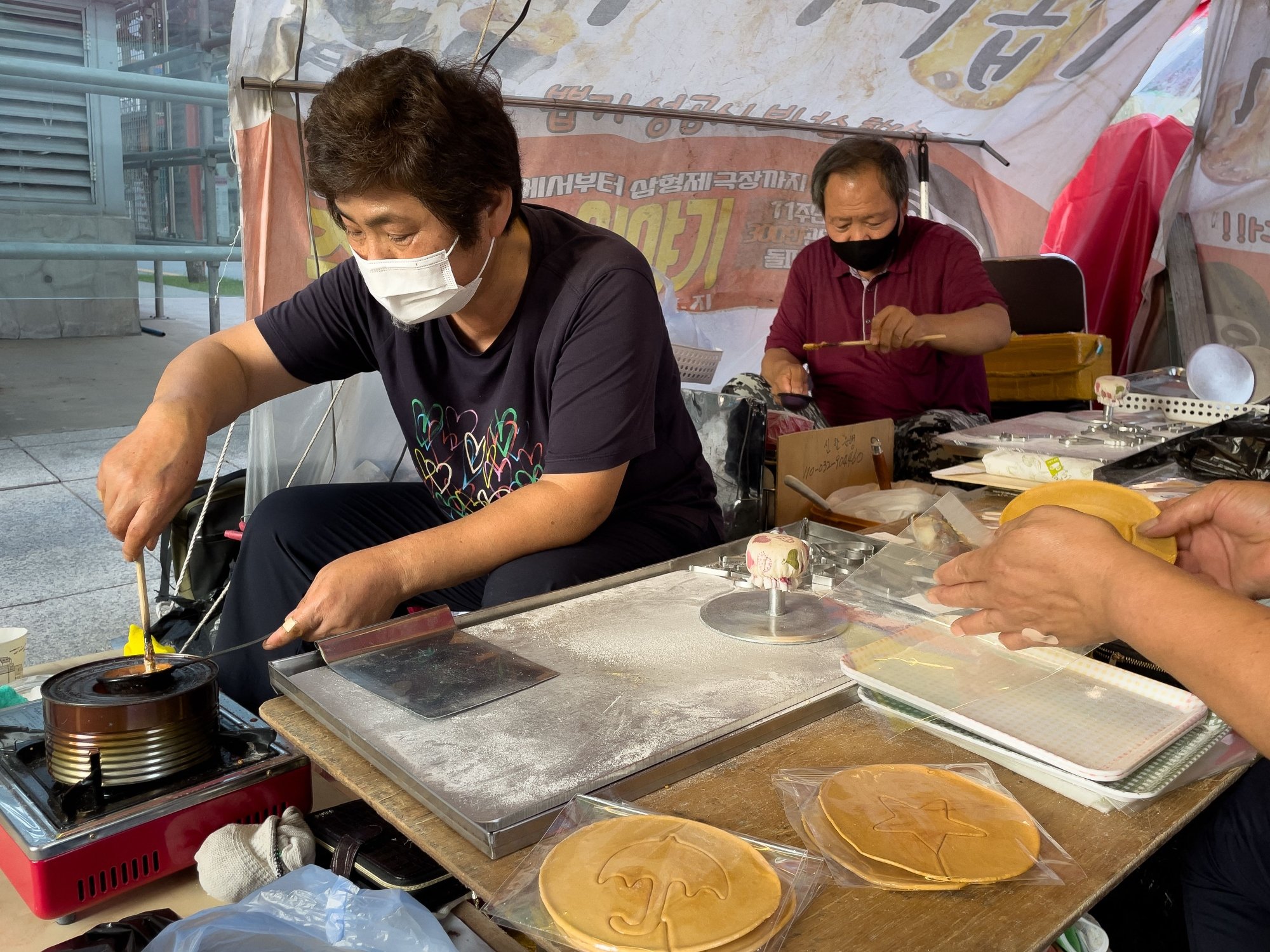 Street vendors Jung Jung-soon (L) and Lim Chang-joo (R) make dalgona candy as seen in Netflix's 'Squid Game.'