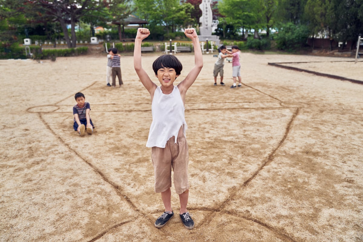 Children play Squid Game at the beginning of the series. A child raises his arms in victory.