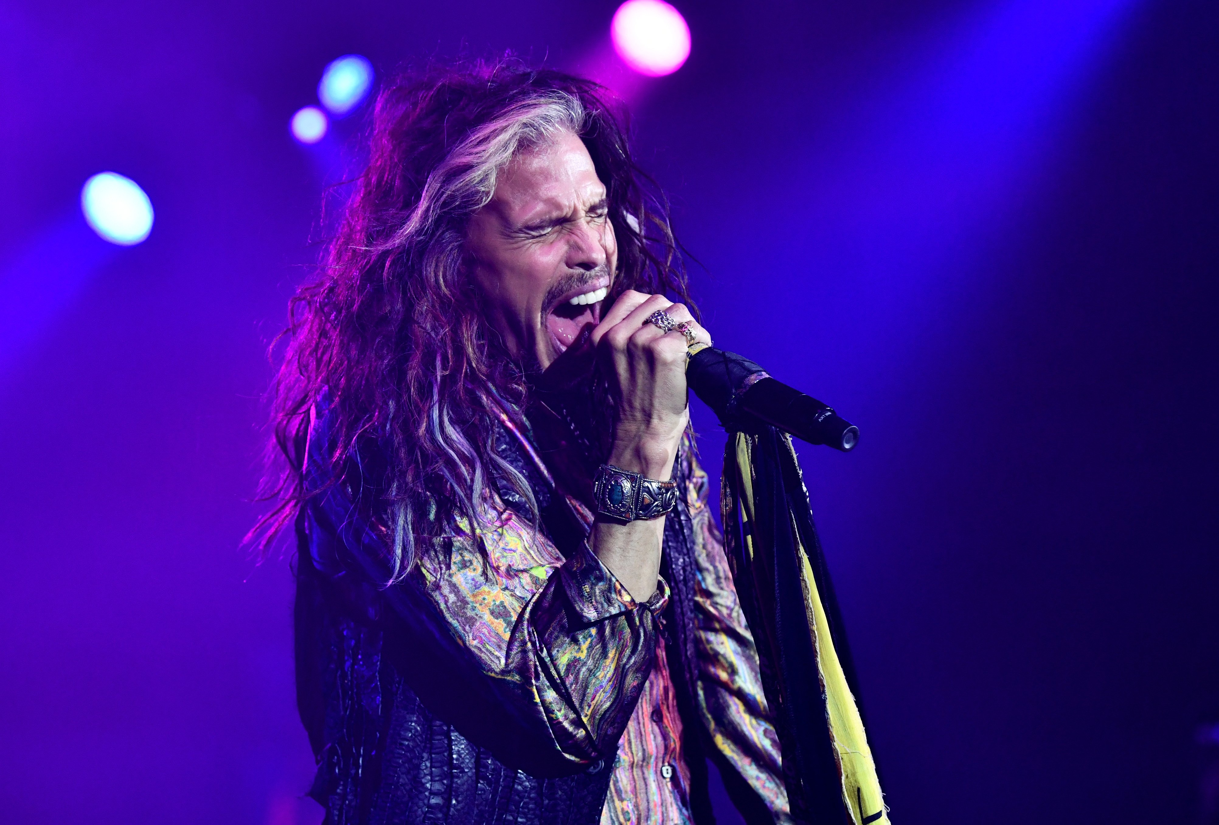 Steven Tyler sings into a microphone during a concert.