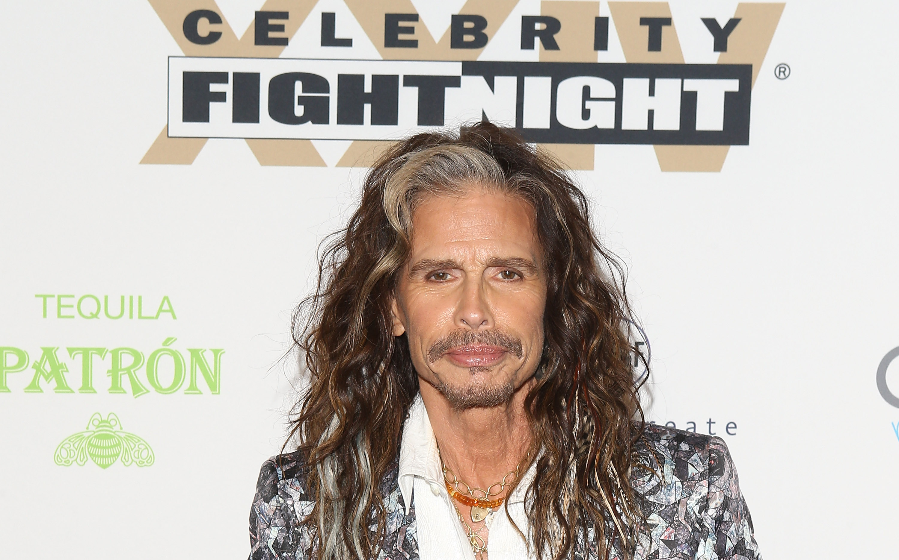 Steven Tyler poses in a white dress shirt and colorful blazer. 