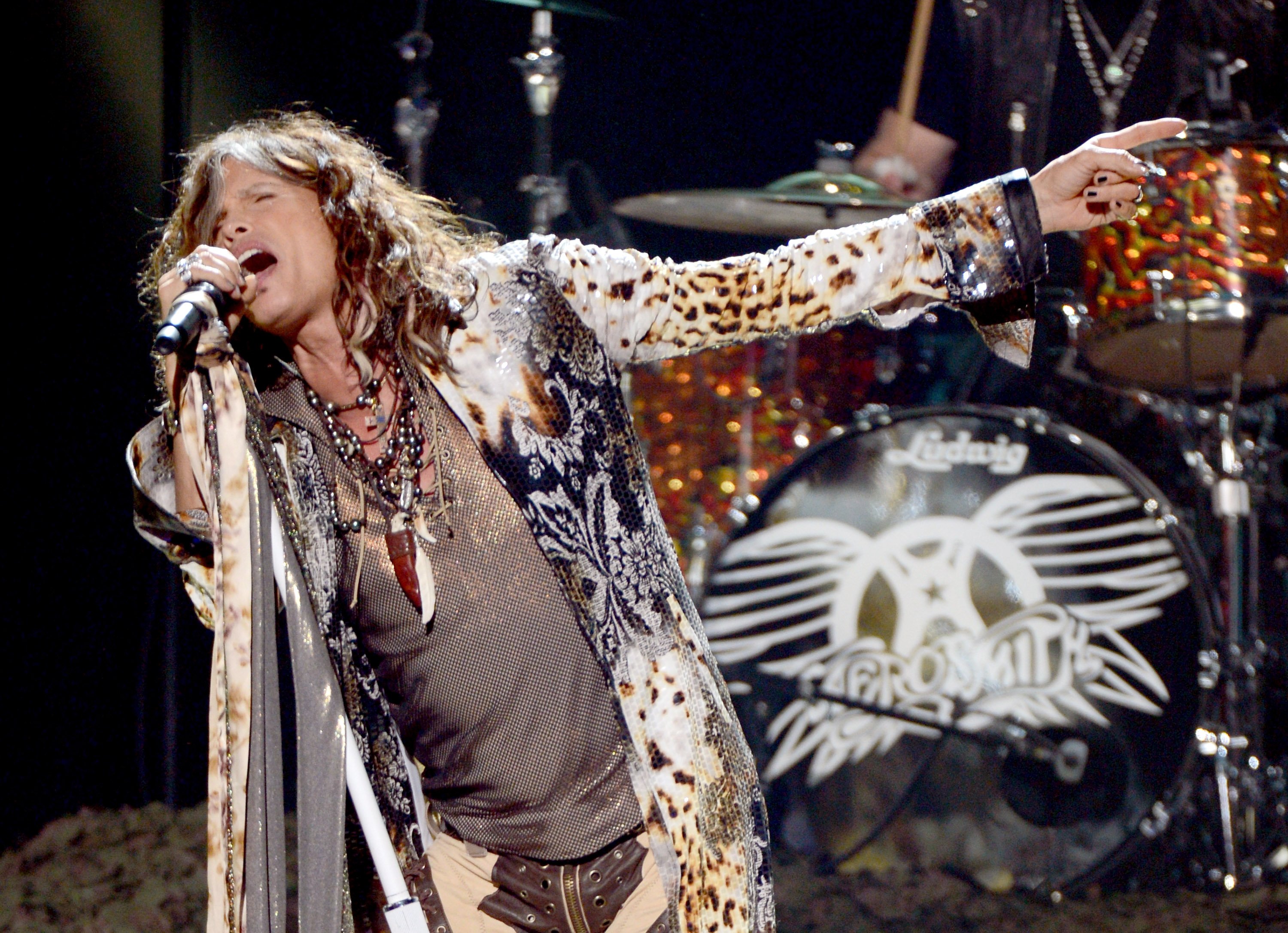 Steven Tyler singing while wearing a leopard print top and pants. 
