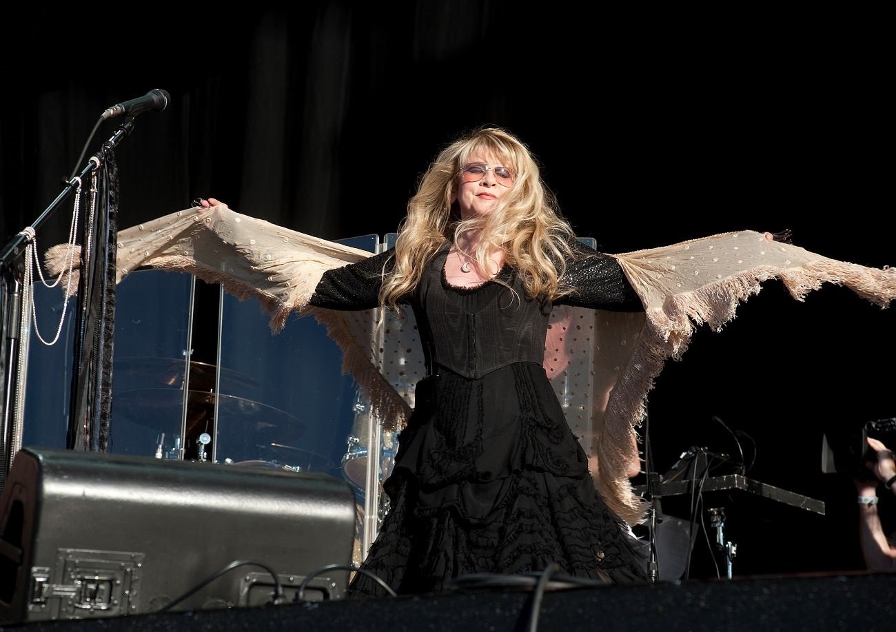 Stevie Nicks wears a black dress and a tan shawl while onstage.
