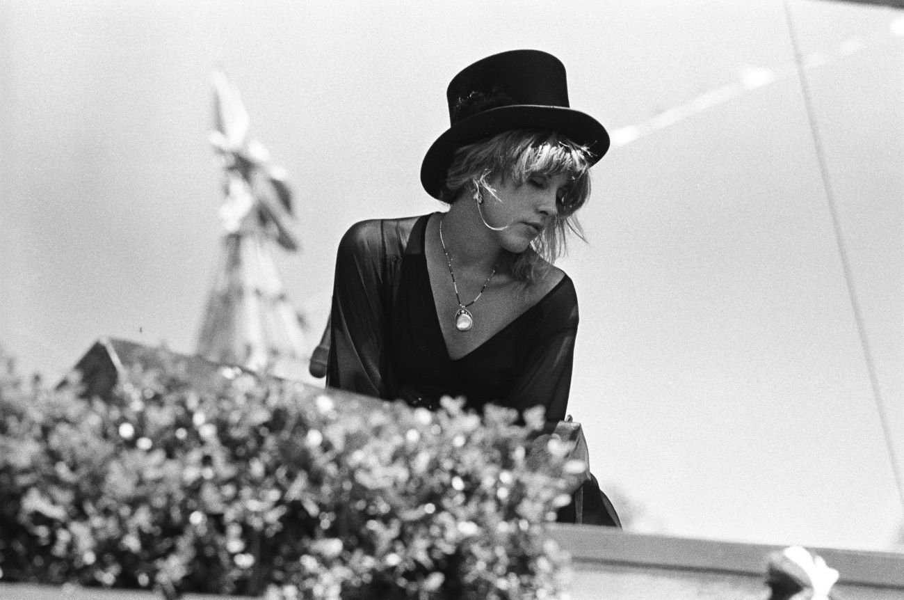 A black and white photo of Fleetwood Mac musician Stevie Nicks wearing a black dress, top hat, and a big silver necklace.