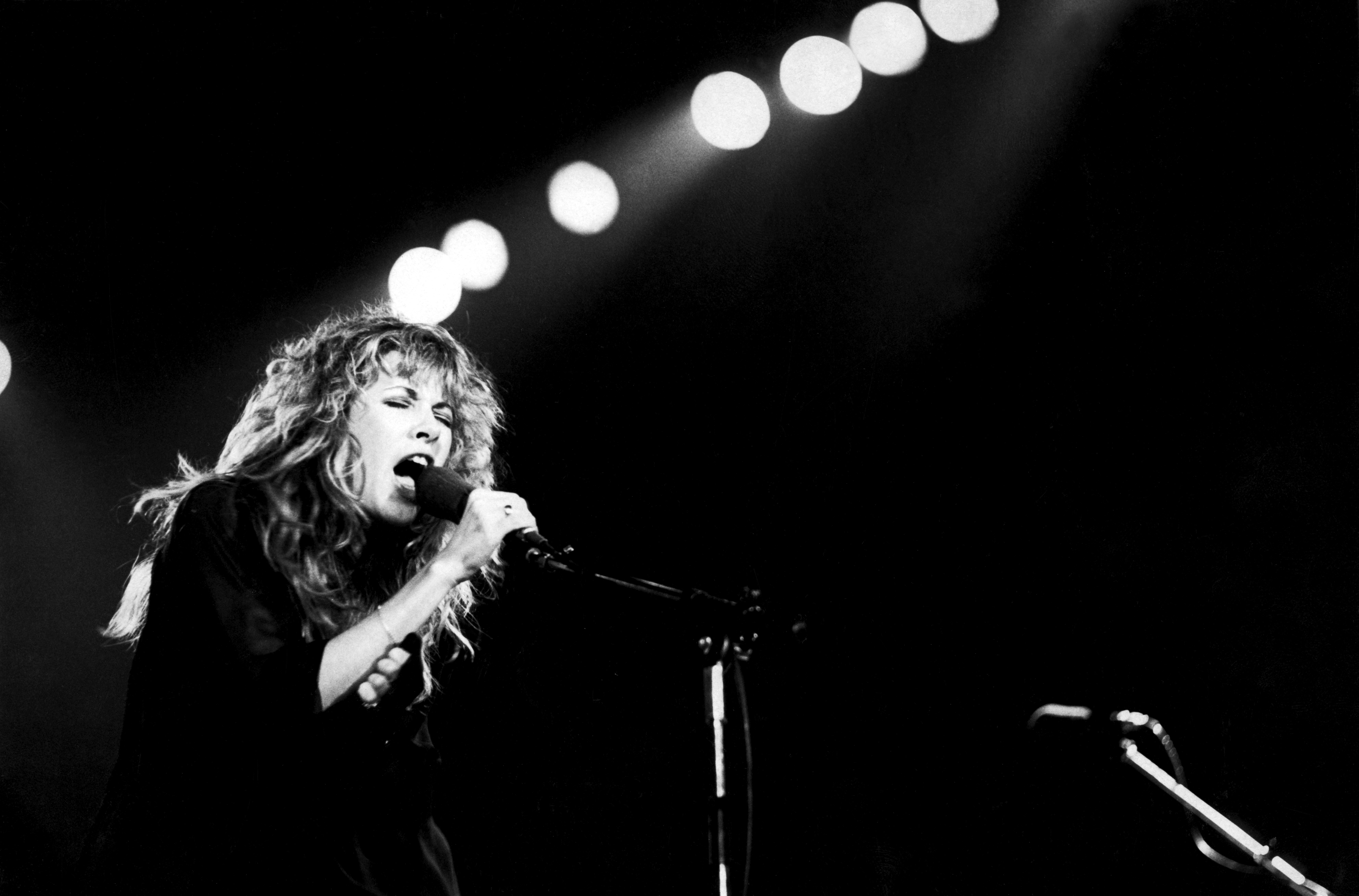 A black and white photo of Stevie Nicks singing into a microphone.