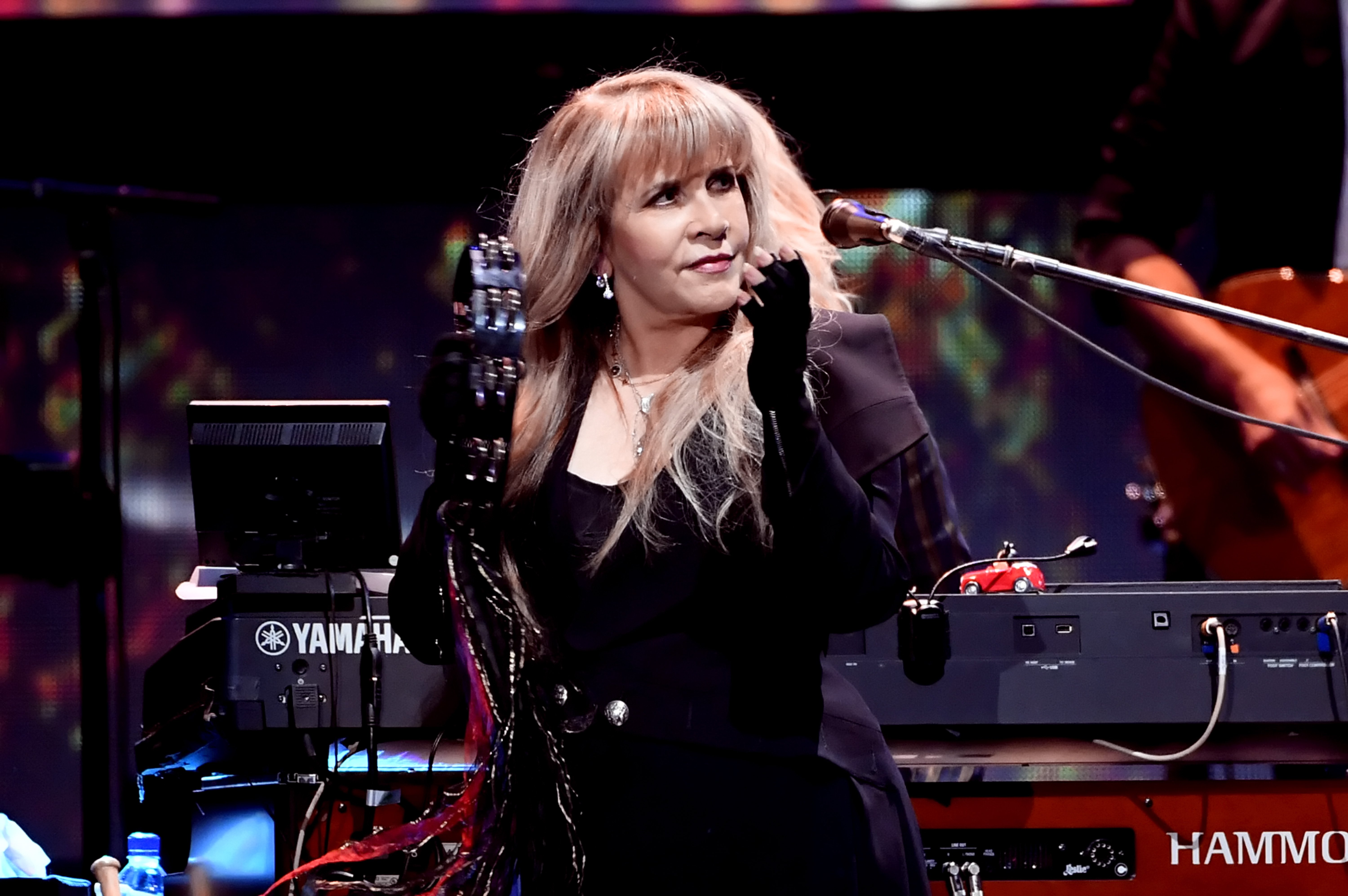 Stevie Nicks wear a black outfit and holds a tambourine.