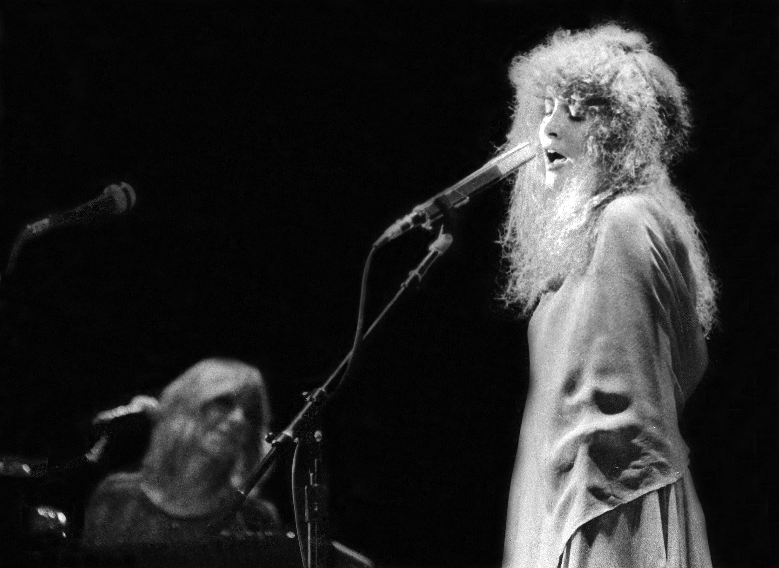 A black and white photo of Stevie Nicks singing in a long dress. 