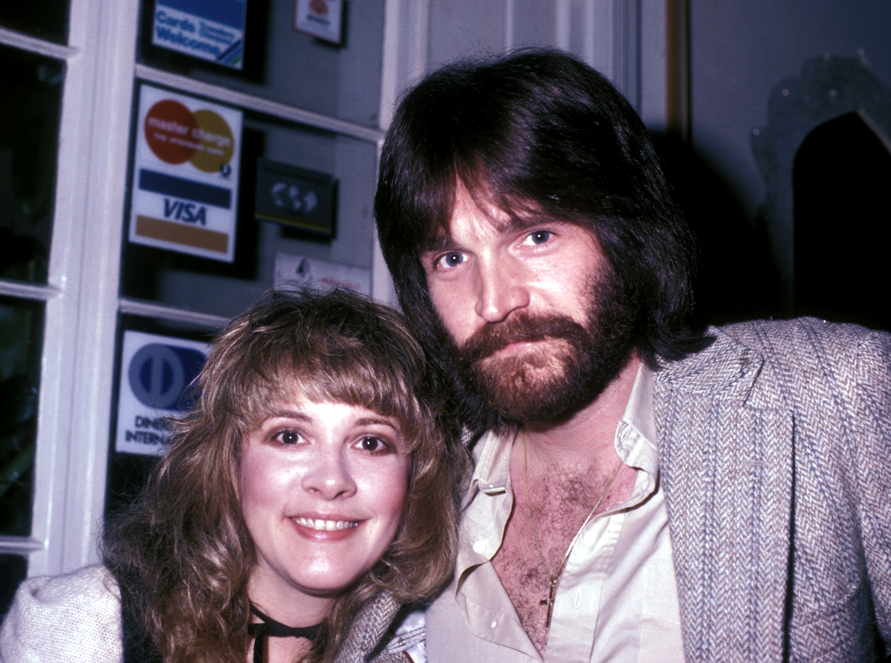 Stevie Nicks poses with her former husband Kim Anderson. She wears a white shirt and he wears a tan suit jacket.