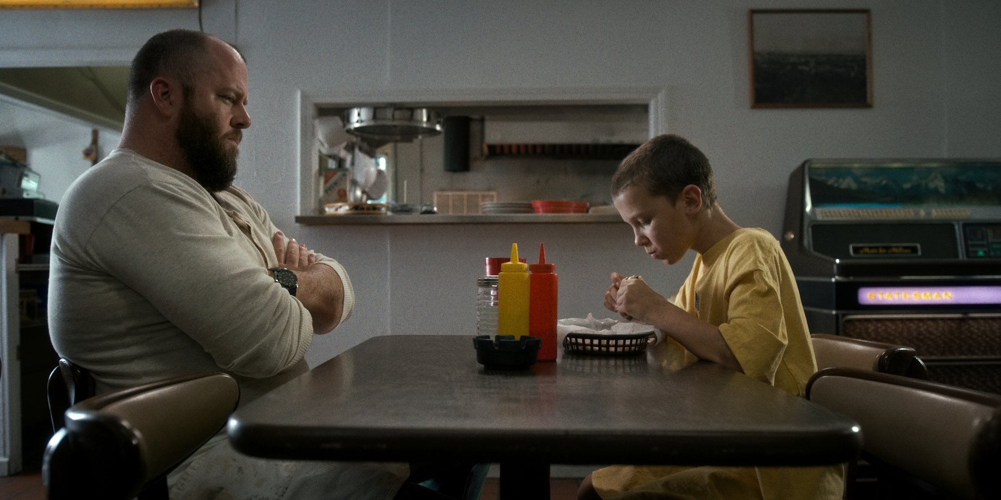 Chris Sullivan as Benny Hammond sitting at a table with Millie Bobby Brown as Eleven in 'Stranger Things' Season 1.