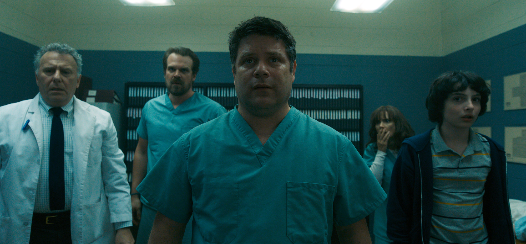 Sean Astin as Bob Newby stands with Joyce Byers, Jim Hopper, and Dr. Owens in the Hawkins lab in a production still from 'Stranger Things' Season 2.