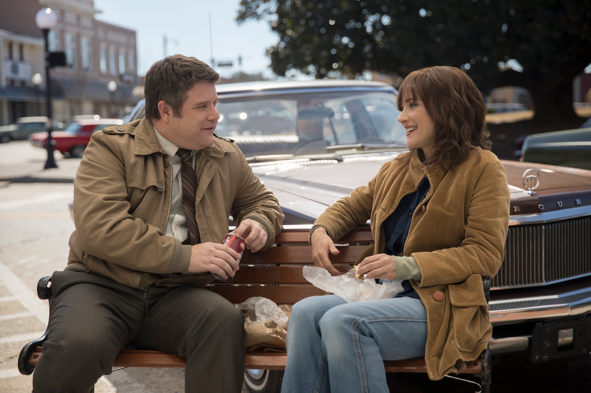 Bob and Joyce sit on a bench outside in a production still from 'Stranger Things' Season 3.