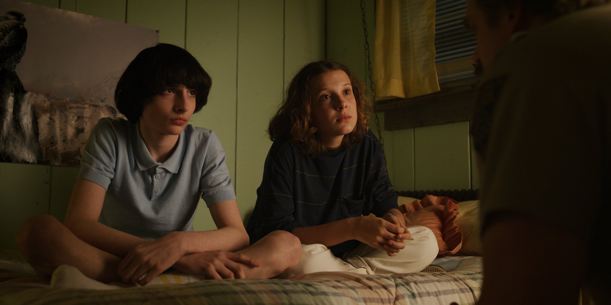 Mike and Eleven sit on her bed in a production still from Stranger Things Season 3.