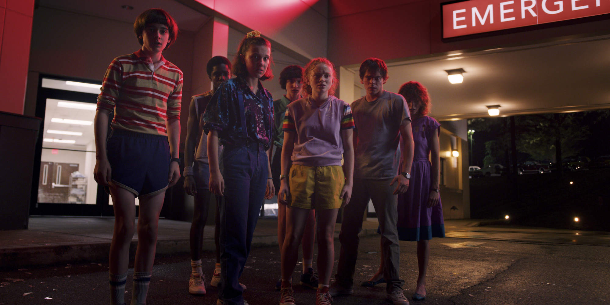 A production still of Millie Bobby Brown, Finn Wolfhard, Caleb McLaughlin, Sadie Sink, Charlie Heaton, and Natalia Dyer standing in Starcourt Mall in Stranger Things Season 3.
