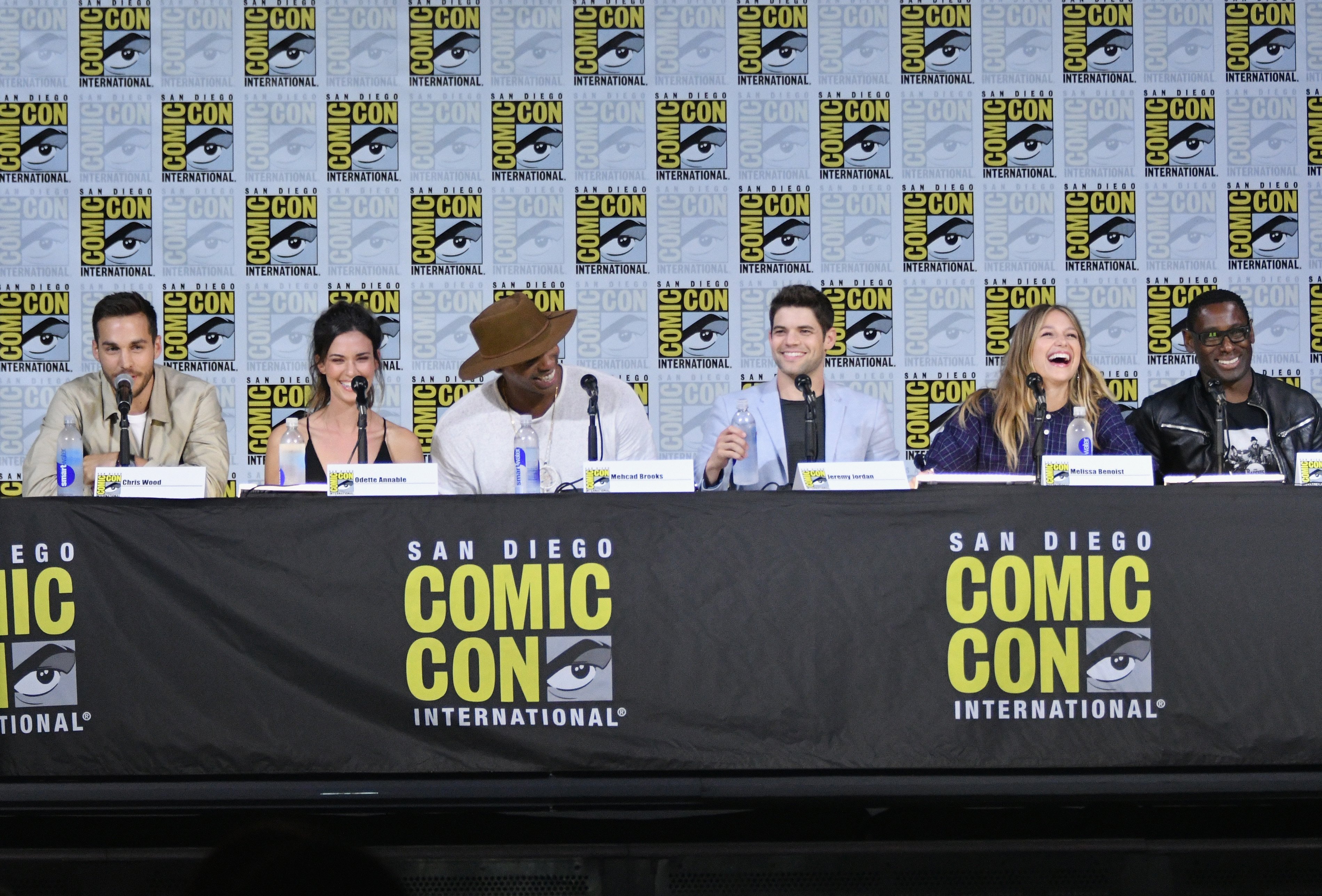 'Supergirl' actors Chris Wood, Odette Annable, Mehcad Brooks, Jeremy Jordan, Melissa Benoist and David Harewood, some of whom will attend DC FanDome 2021, laugh during a San Diego Comic-Con panel where they all sit behind their namecards.