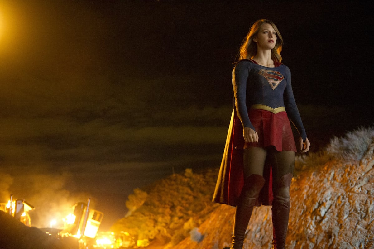 Kara Danvers in the Supergirl suit in front of a fire