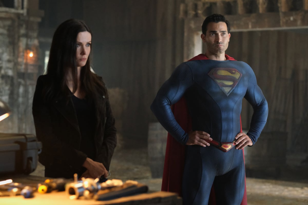 'Superman & Lois' stars Bitise Tulloch and Tyler Hoechlin, in character, stand side-by-side. Tulloch wears a black jacket over a black shirt. Hoechlin wears the Superman suit.