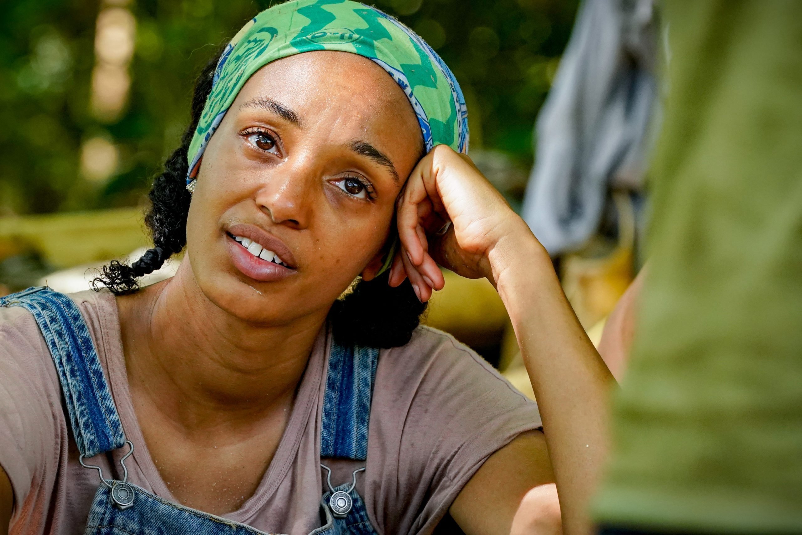 Shantel Smith on 'Survivor 41' wears a shirt and overalls as she sits down on the ground.
