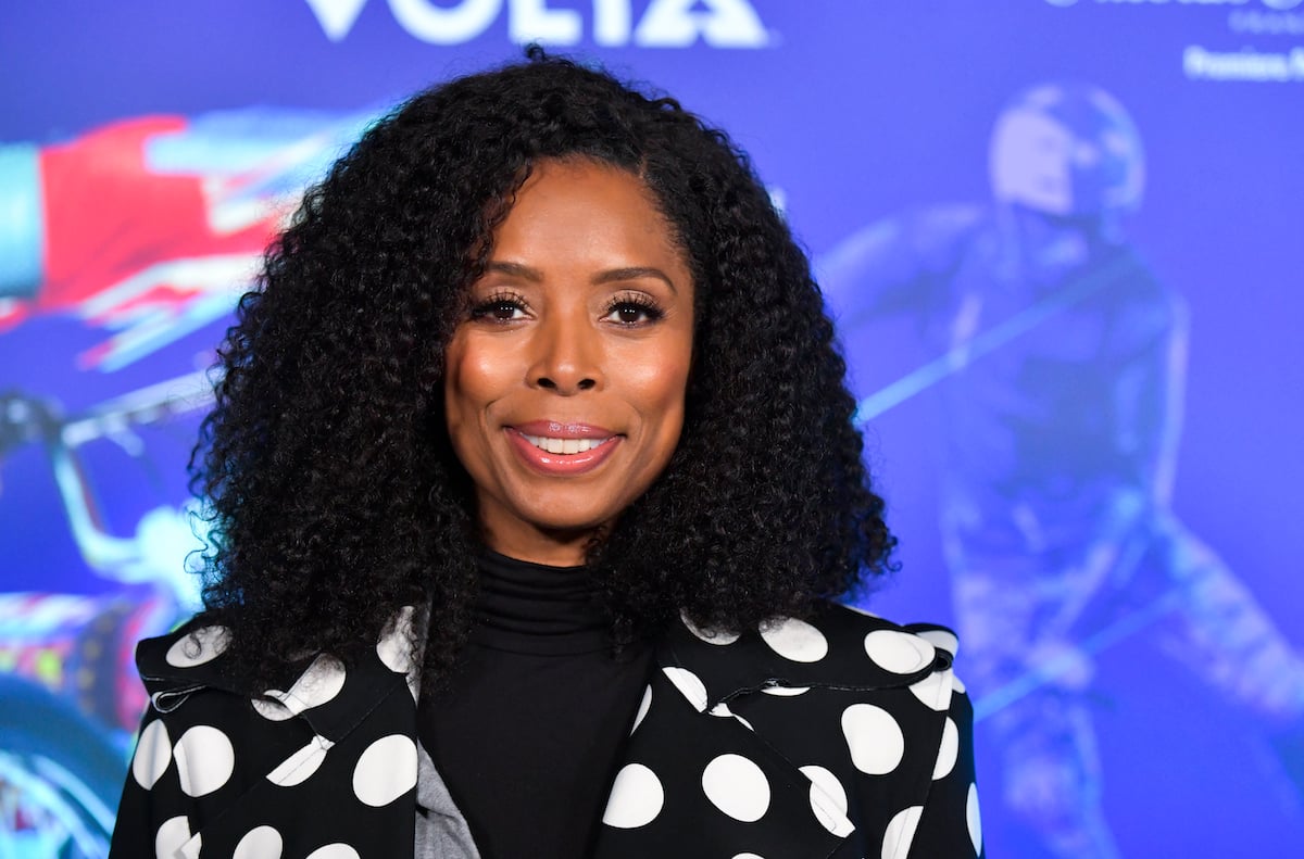 Tasha Smith smiles while wearing a black and white jacket