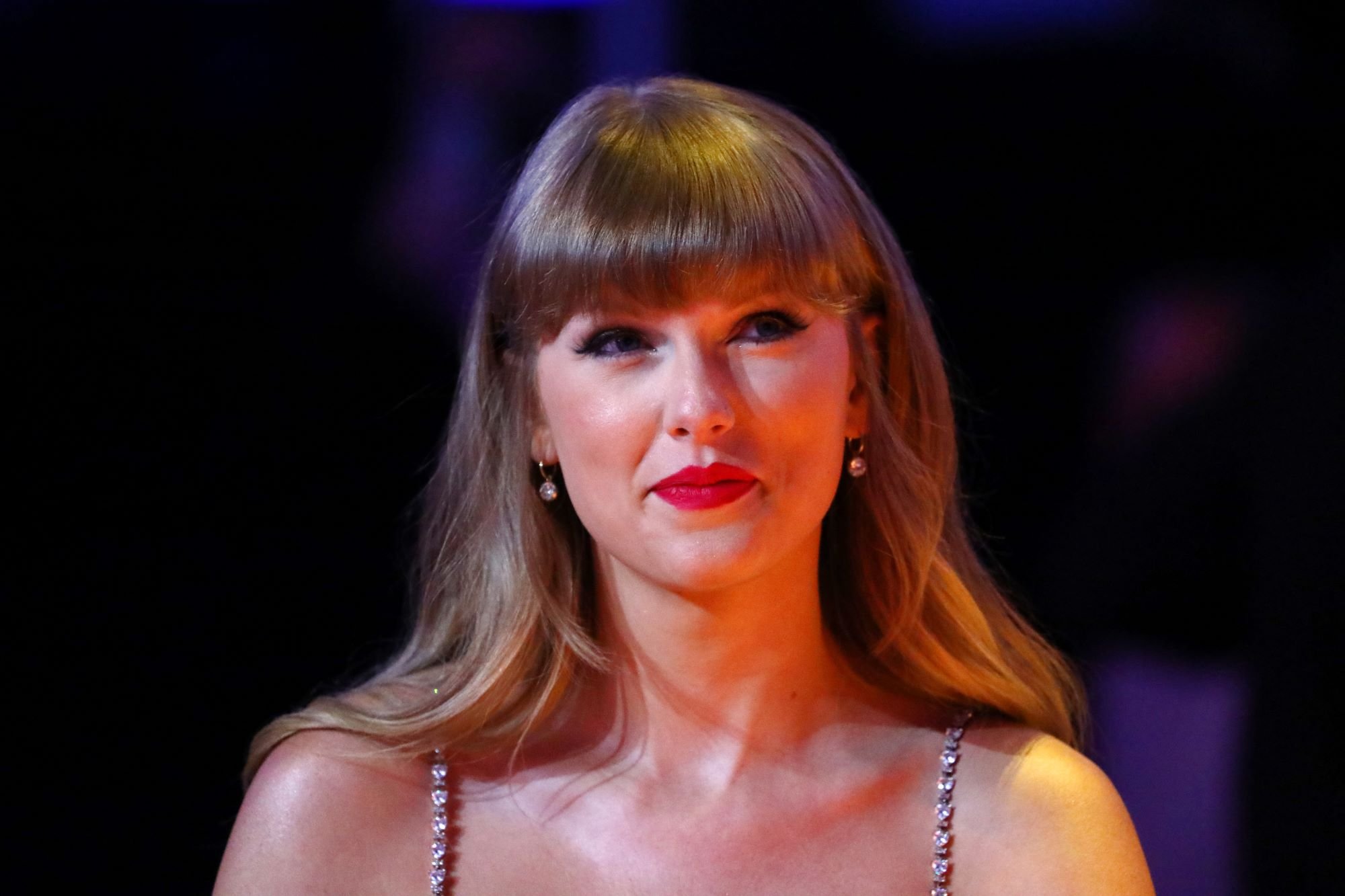 Taylor Swift with a think diamond studded strap in front of a black background.