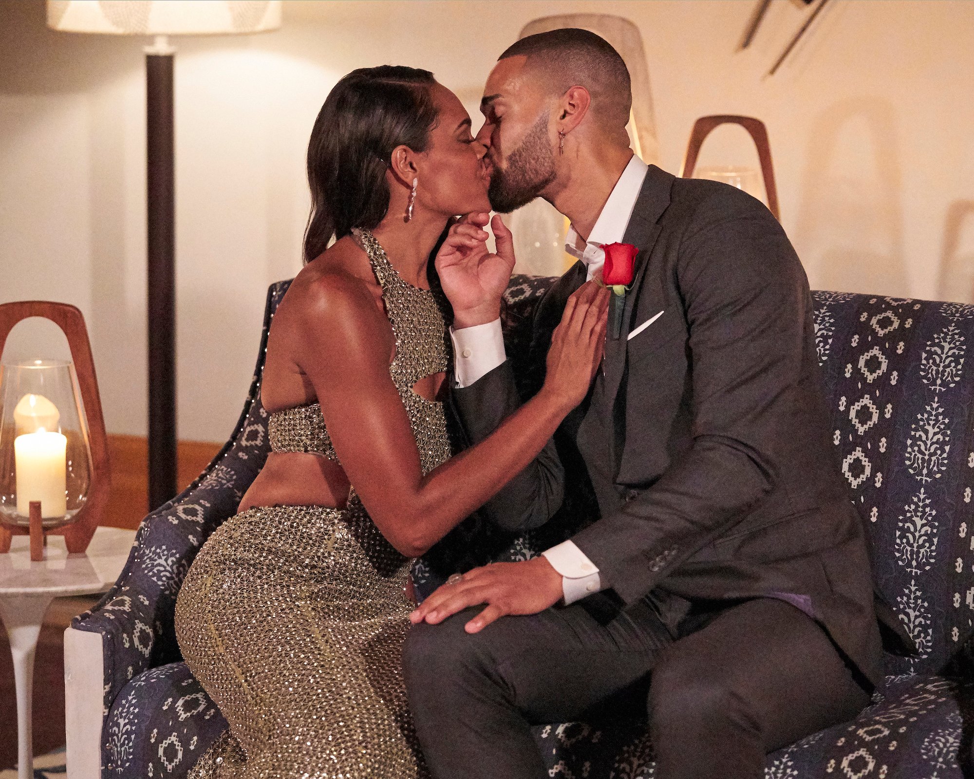 Michelle Young in a gold dress kissing Nayte Olukoya in a suit while sitting on a couch in a production still from 'The Bachelorette' Season 18. Nayte received the First Impression Rose on the first night.