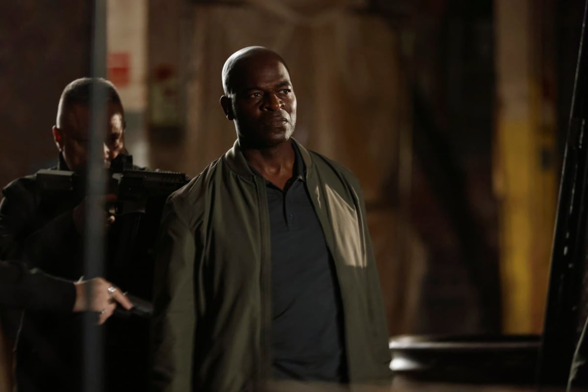 Hisham Tawfiq as Dembe Zuma in The Blacklist Season 9. Dembe is wearing a jacket and blue polo. 