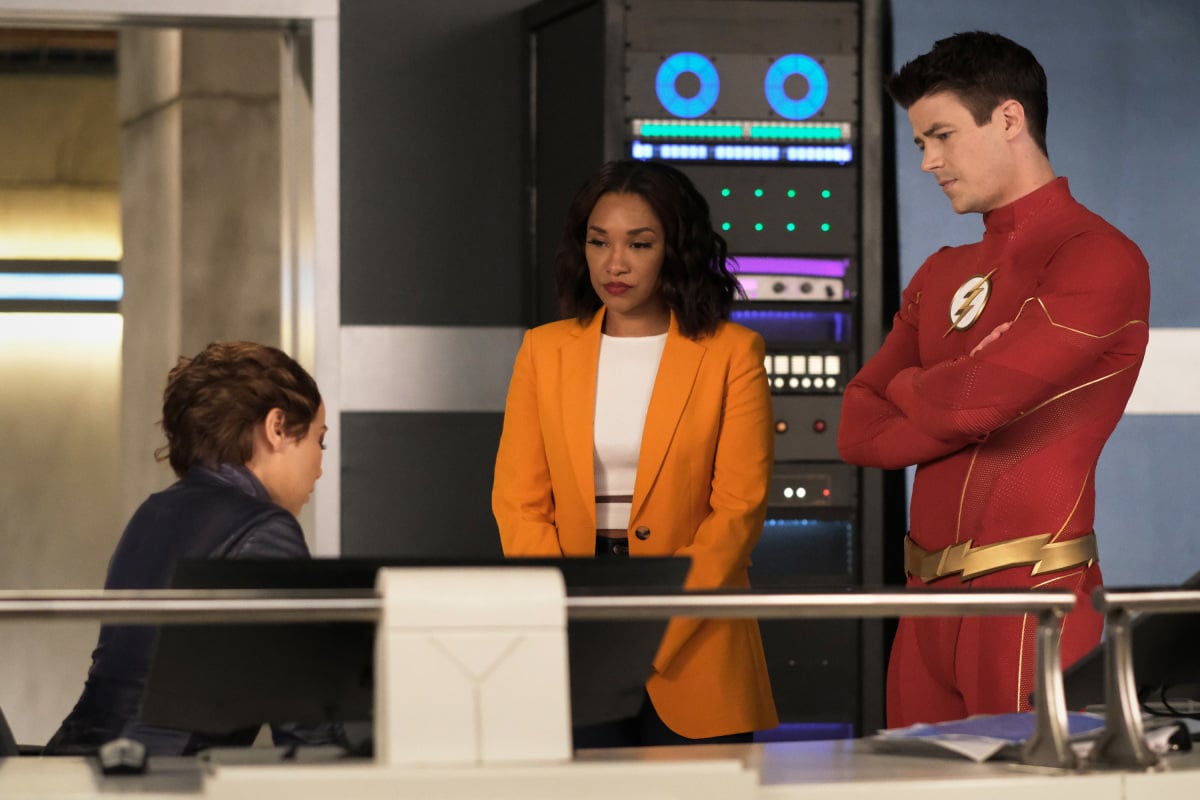 'The Flash' Season 8 stars Jessica Parker Kennedy, Candice Patton, and Grant Gustin, in character, gather in S.T.A.R. Labs. Kennedy wears her character's XS costume. Patton wears a yellow suit jacket over a white shirt. Gustin wears his character's Flash costume.