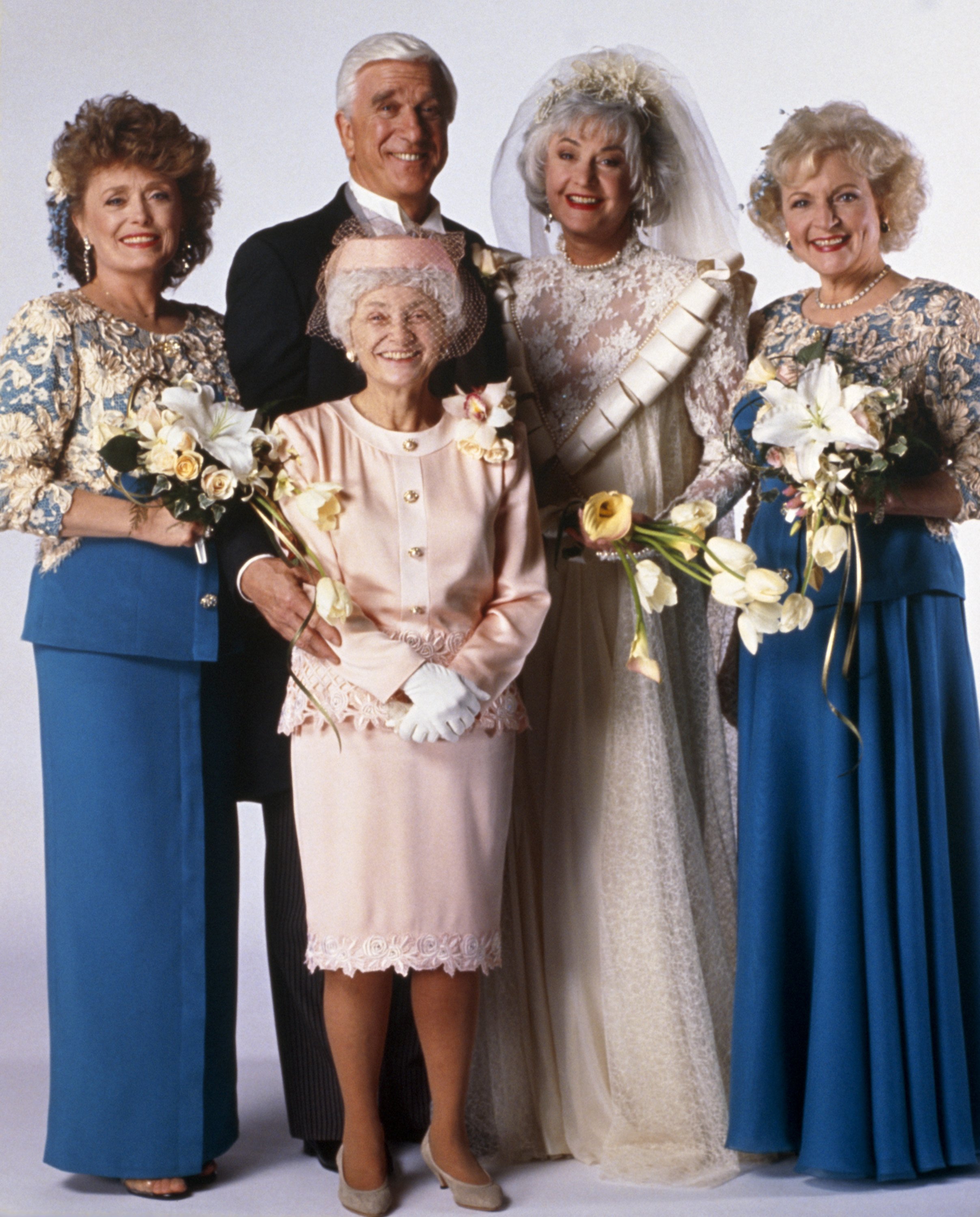 Rue McClanahan in a blue bridesmaid dress, Estelle Getty in a pink dress, Leslie Nielsen in a tuxedo, Bea Arthur in a white wedding dress, and Betty White in a blue bridesmaid dress in a photo from 'The Golden Girls.'