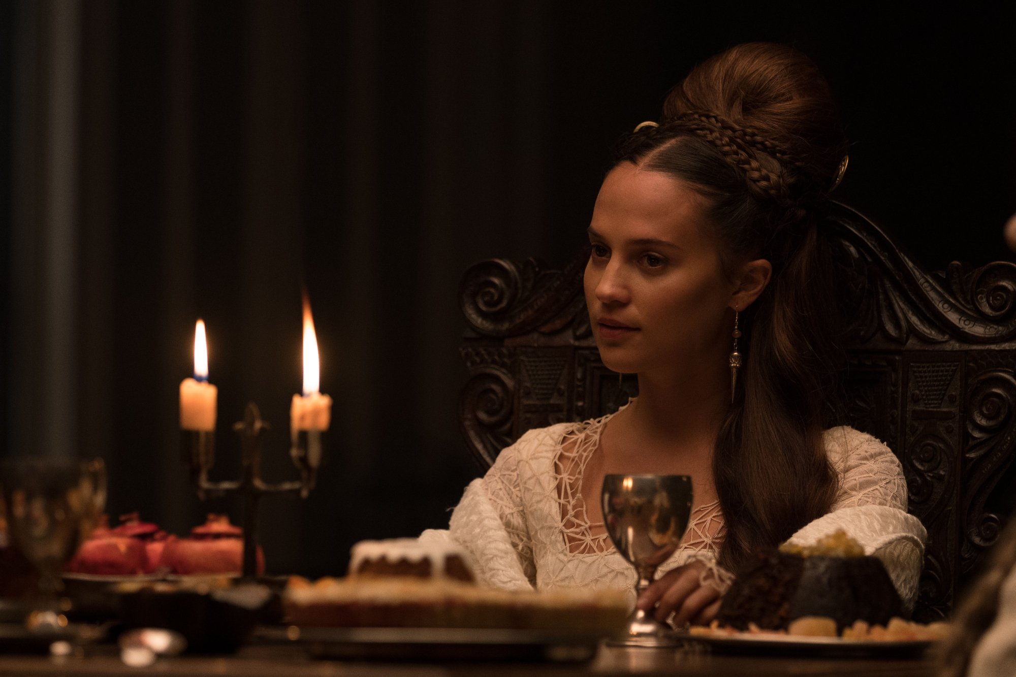 'The Green Knight' actor Alicia Vikander as the Lady sitting at a candlelit table with a wine goblet