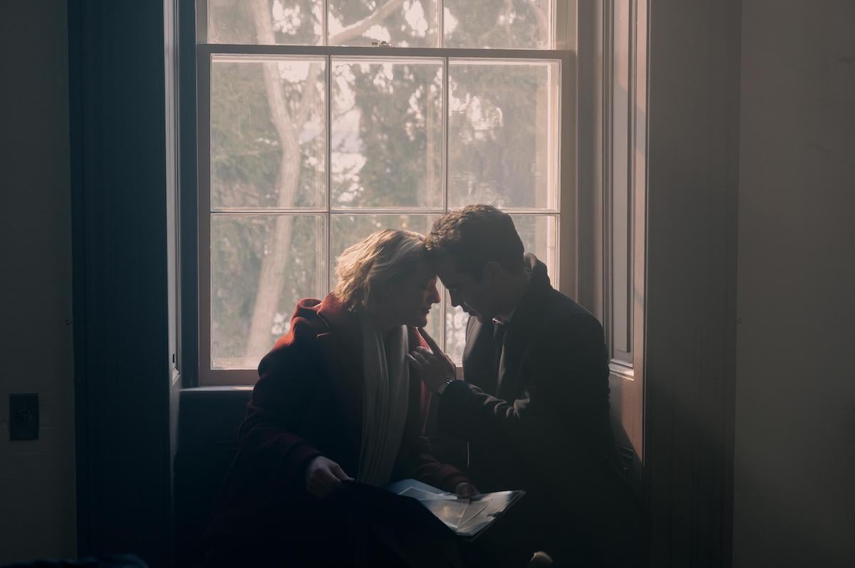 June and Nick leaning together, sitting in a window seat