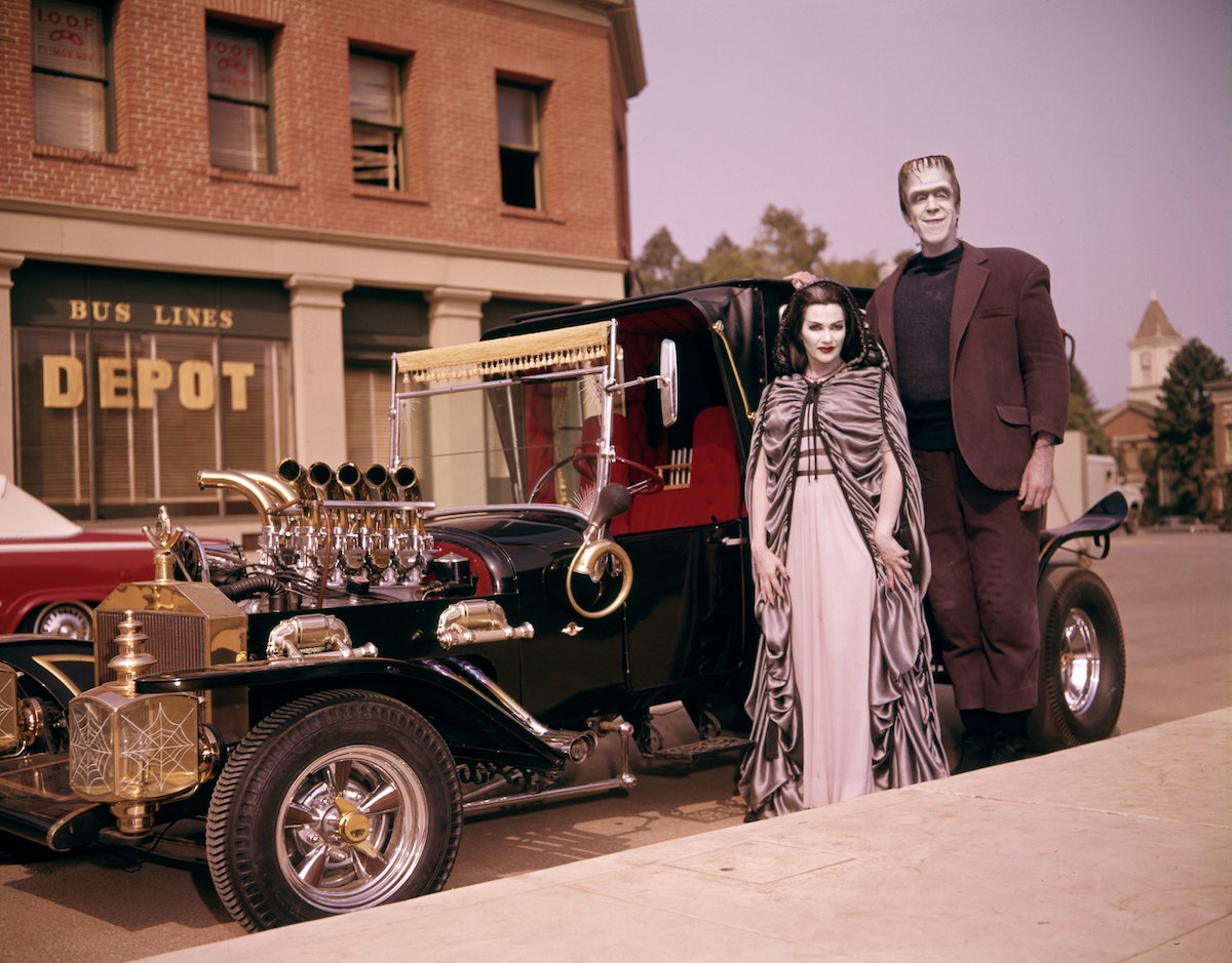 Color photo of Lily and Fred Munster from 'The Munsters' standing in front of the Munster Koach