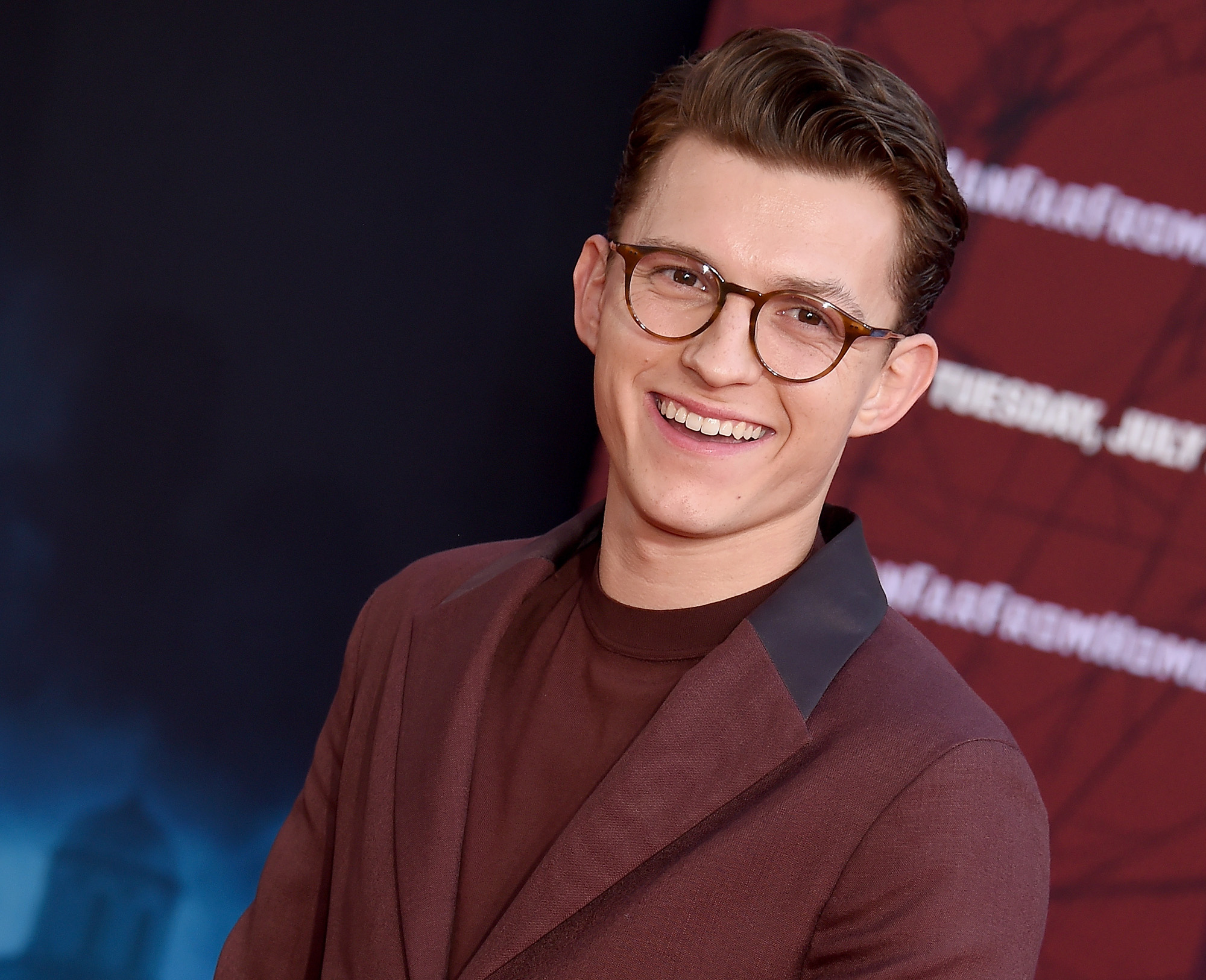 Tom Holland, who will star as Nathan Drake in Sony's 'Uncharted' movie. He's wearing a brown suit and glasses, and his hair is slicked back.