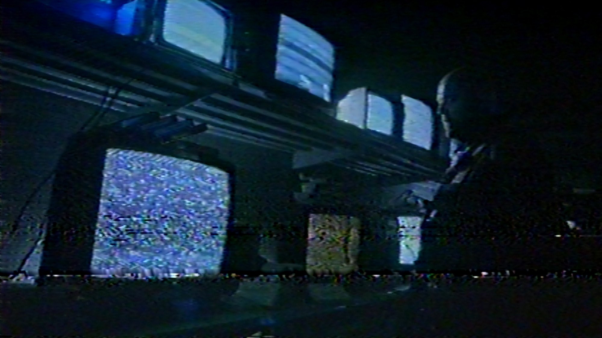 'V/H/S/94' horror movie installment 'Holy Hell' standing in front of static televisions