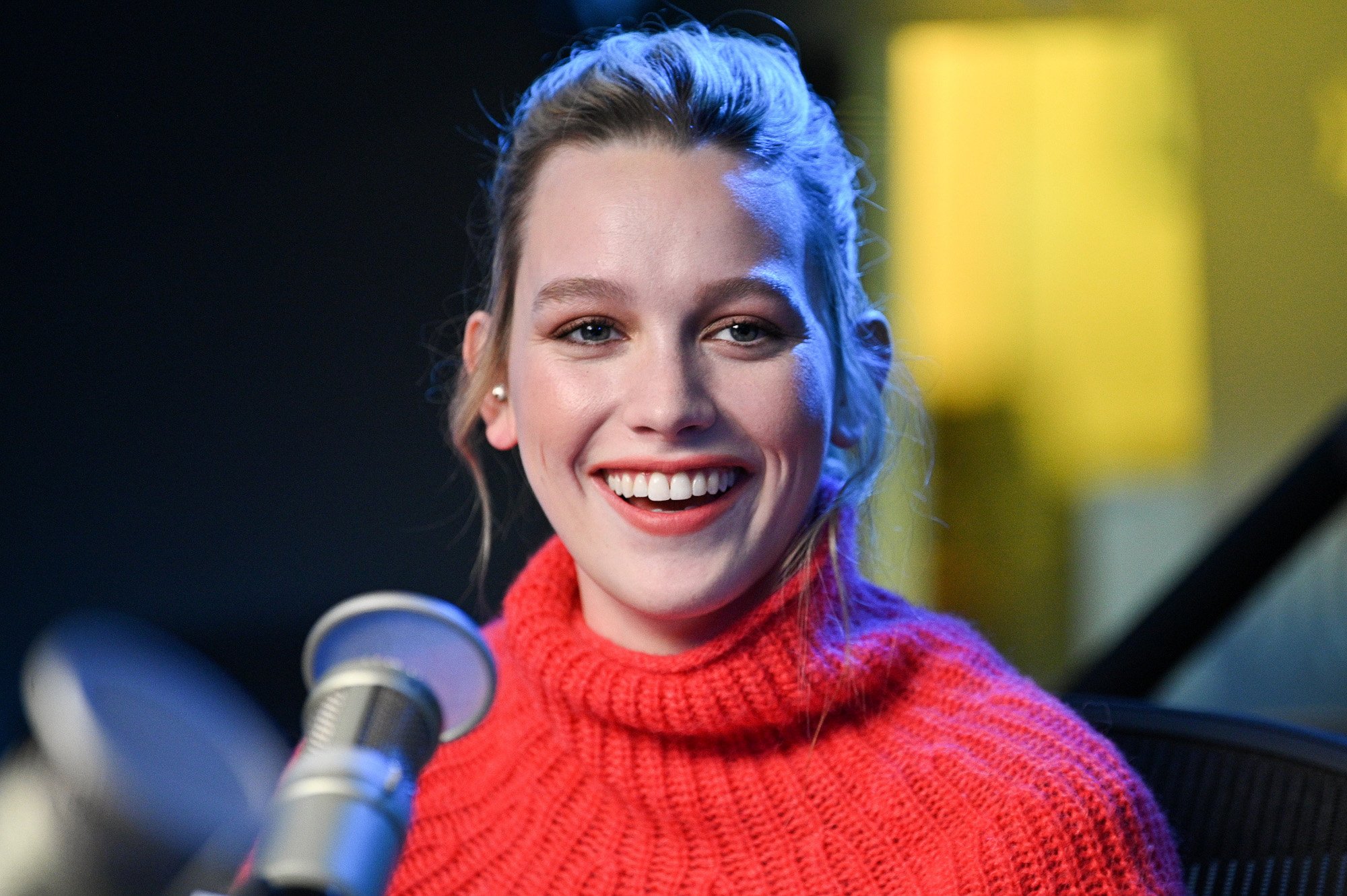 'You' Season 3 star Victoria Pedretti. She's wearing a pink turtle neck sweater, her hair is pulled back, and she's smiling.