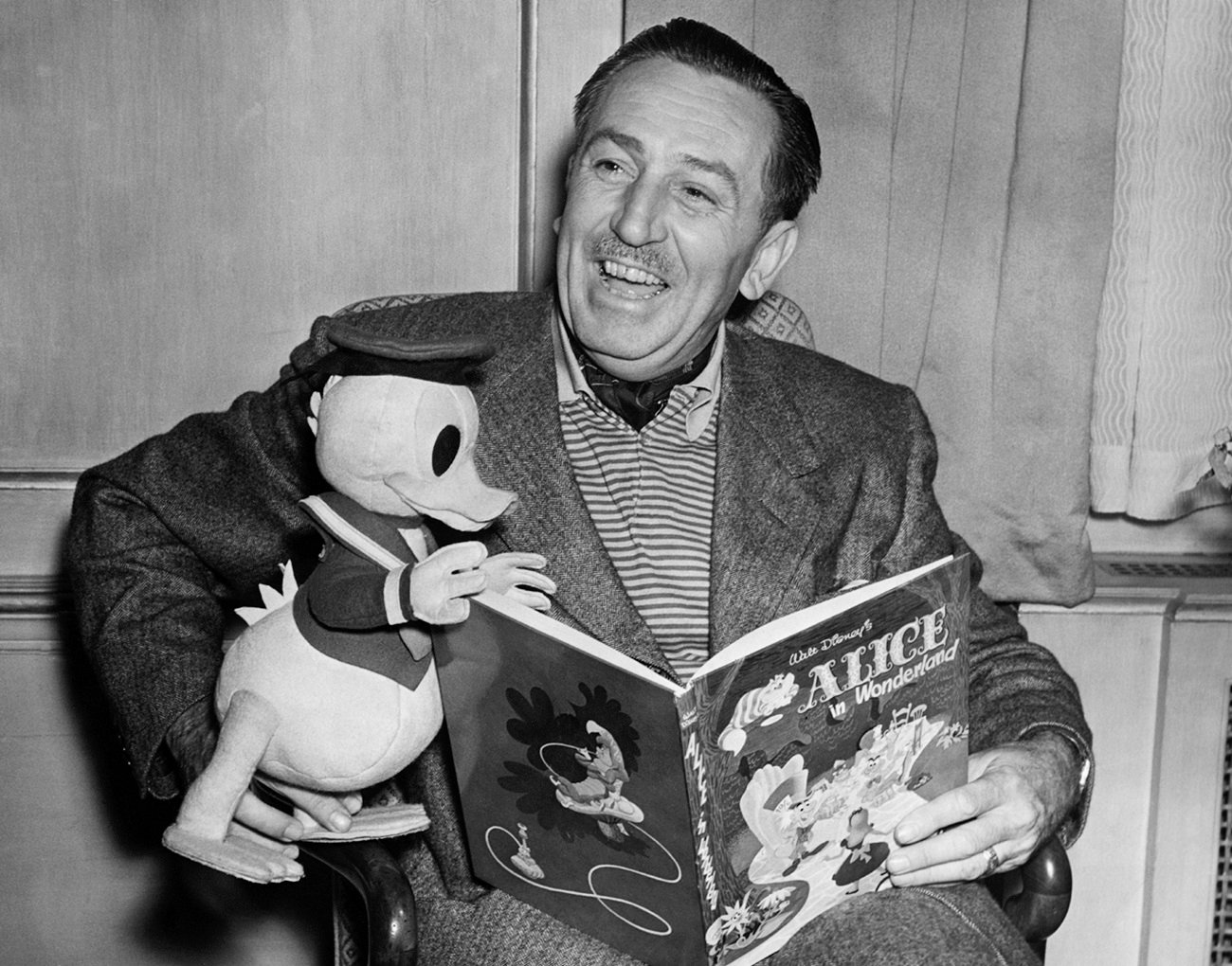 Walt Disney sits with a Donald Duck toy and an 'Alice in Wonderland' book.